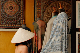 Person wearing a conical hat near patterned textiles and mannequins.