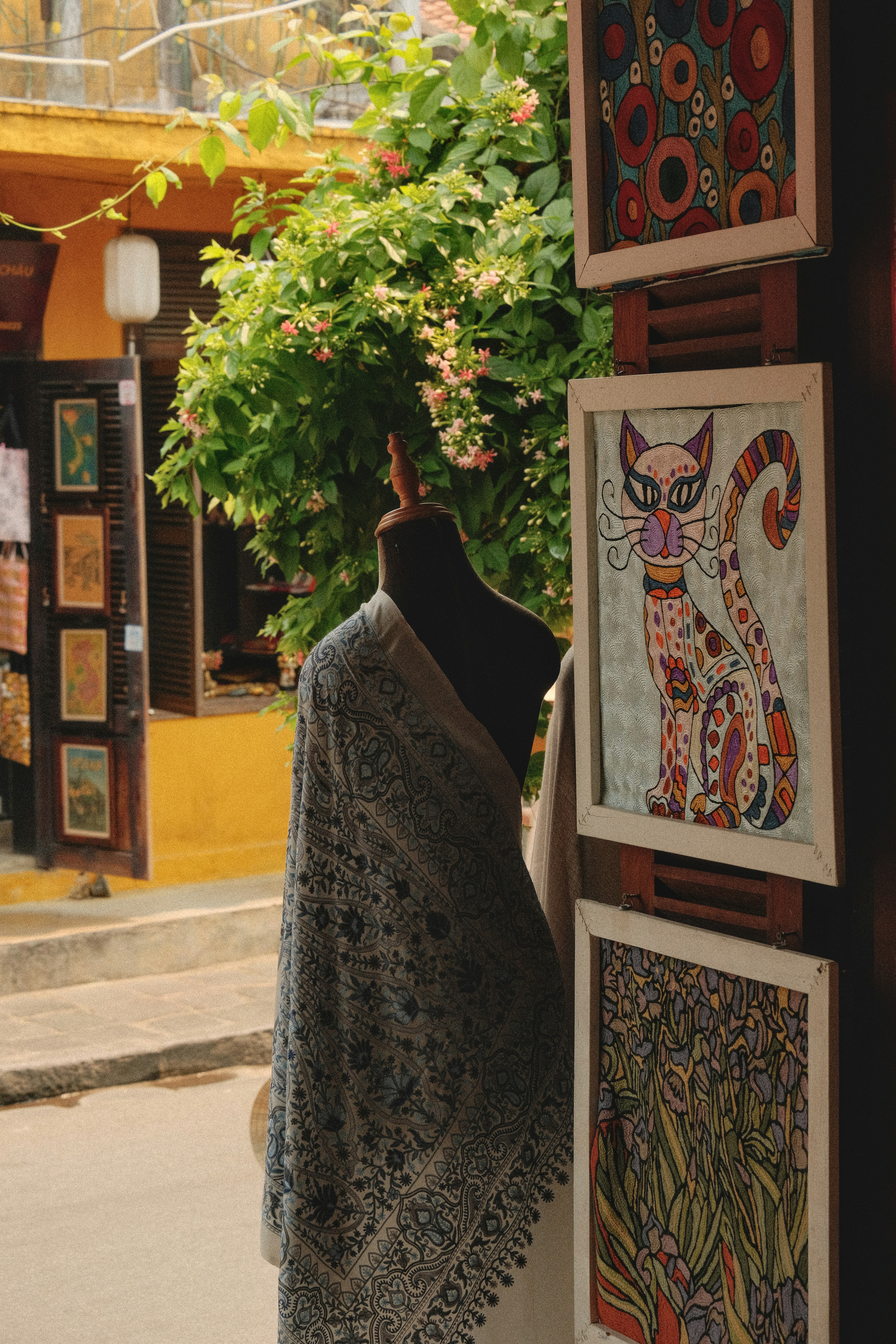 Schaufensterpuppe mit Schal und bunten Katzenkunstwerken in einer Gasse.