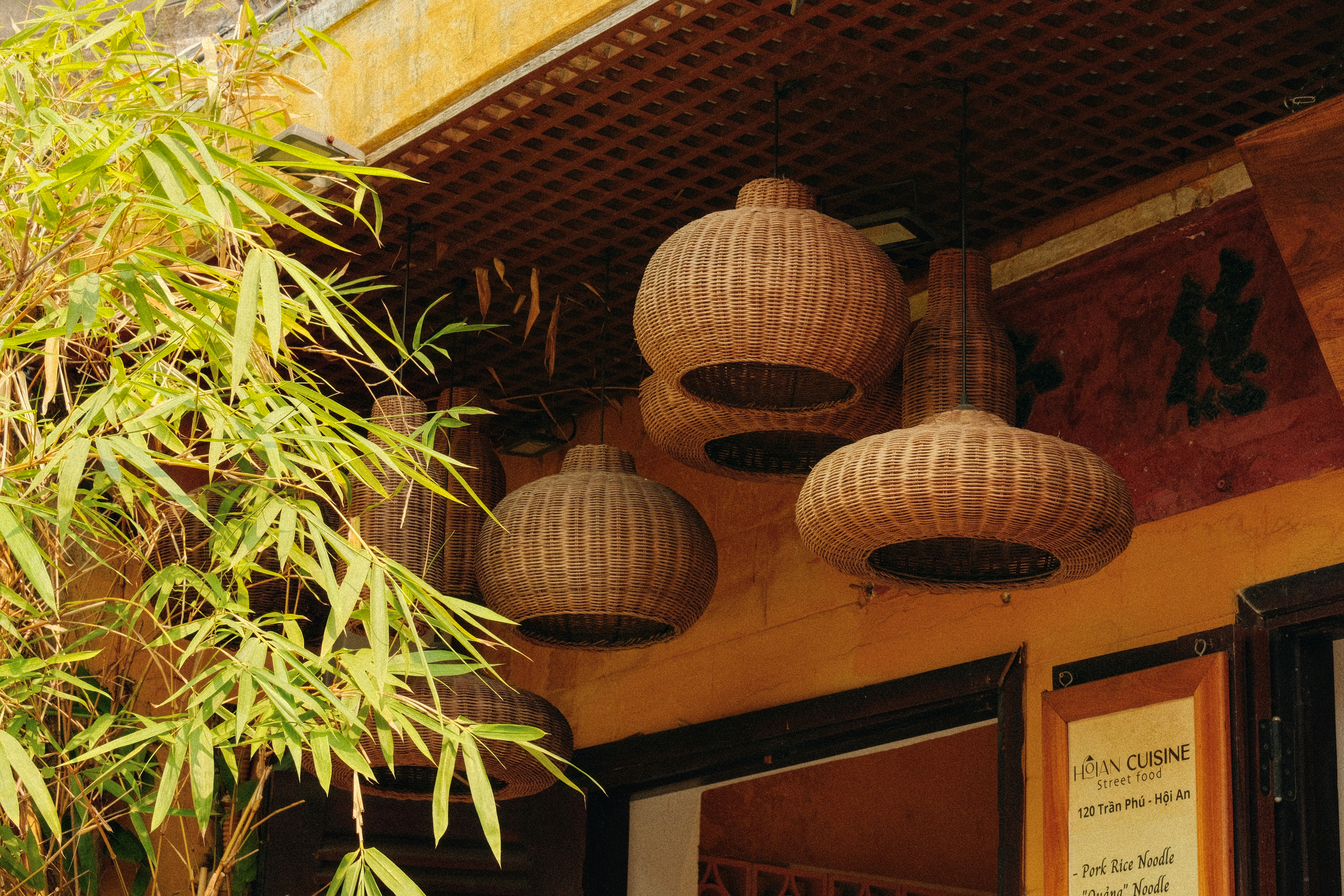 Woven rattan light fixtures hang near green bamboo leaves.