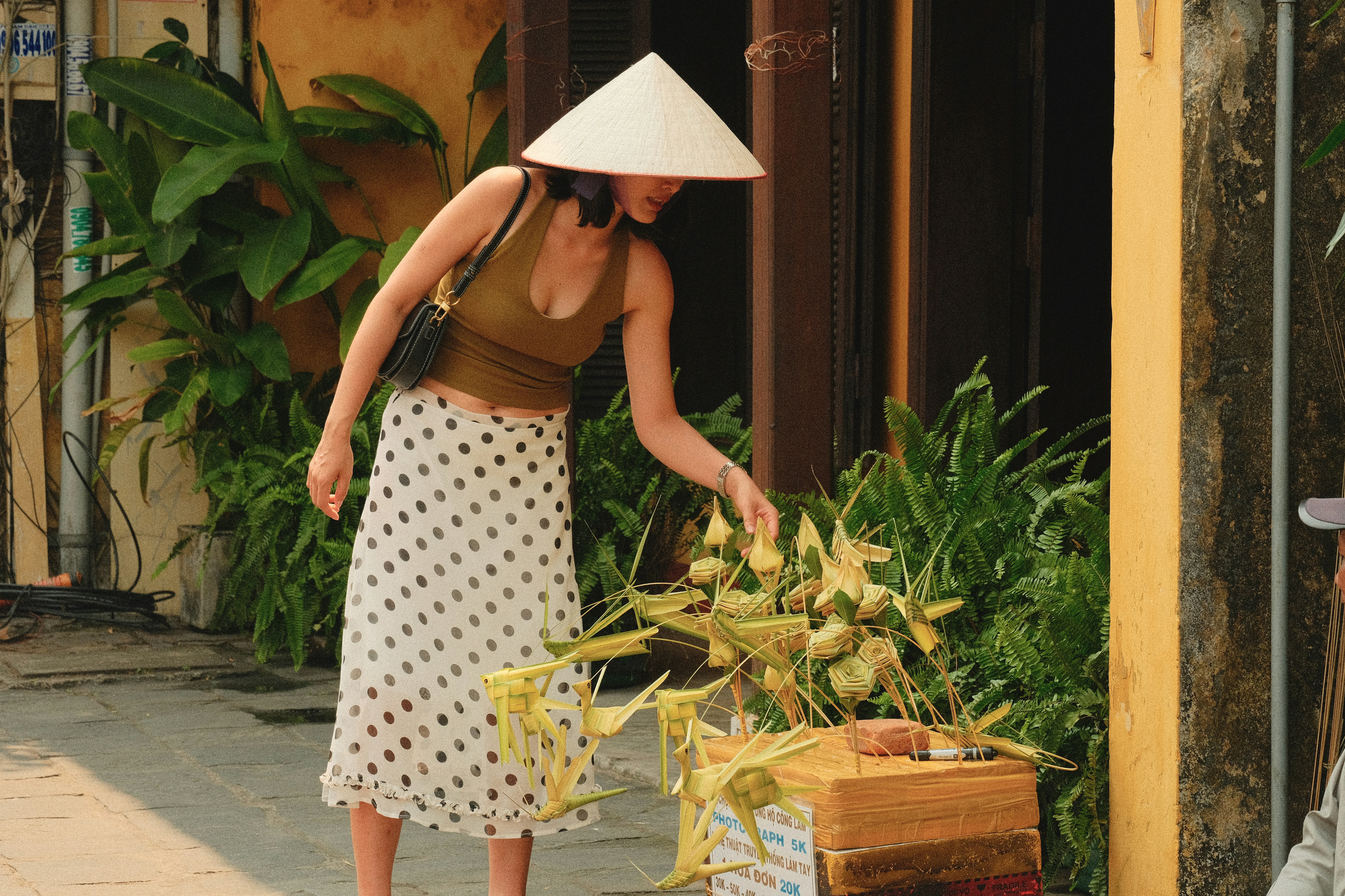 Woman in conical hat examines decorative items.