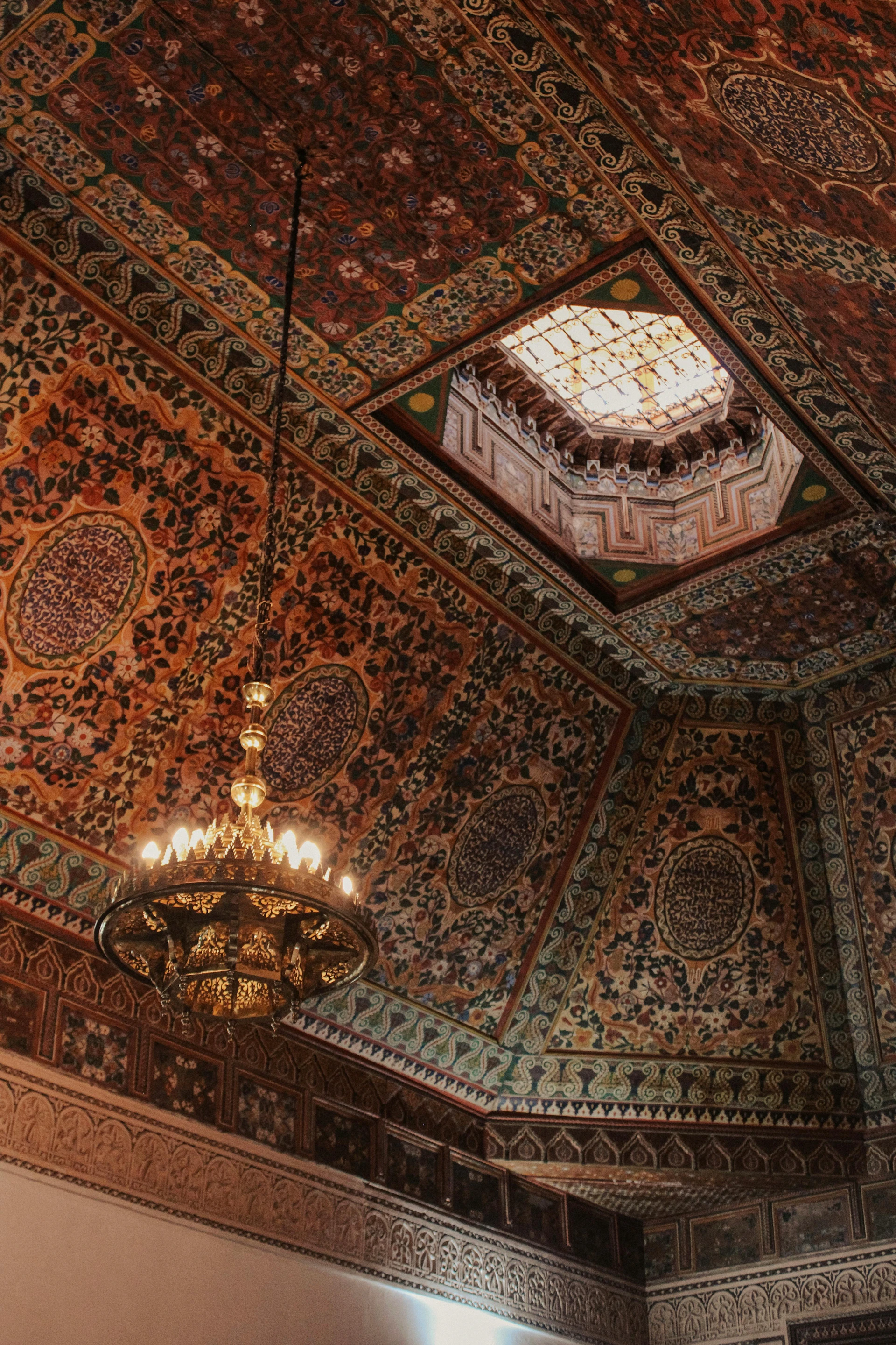 Ornate patterned ceiling with a chandelier and a skylight.
