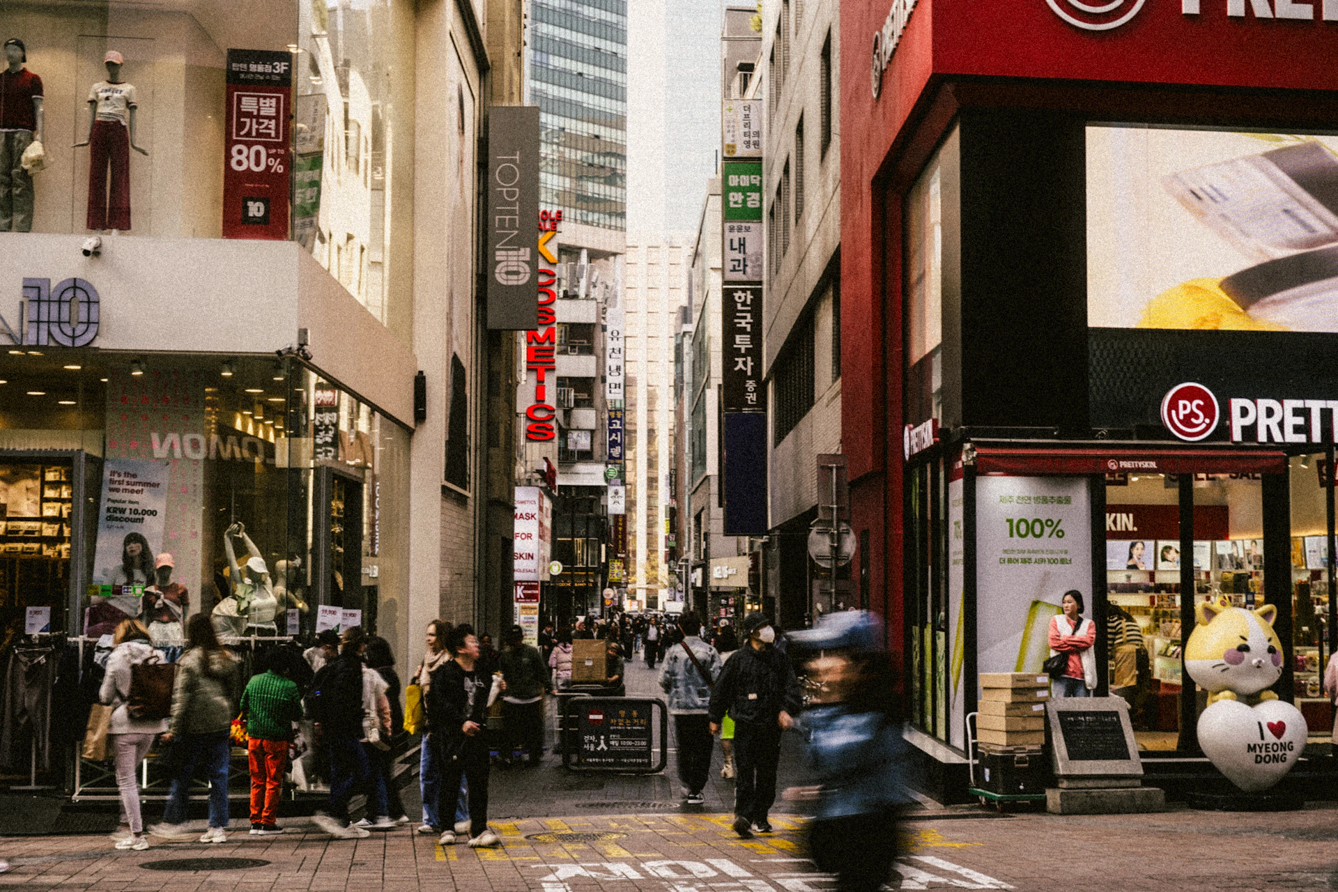 People walking down a busy city street with shops.
