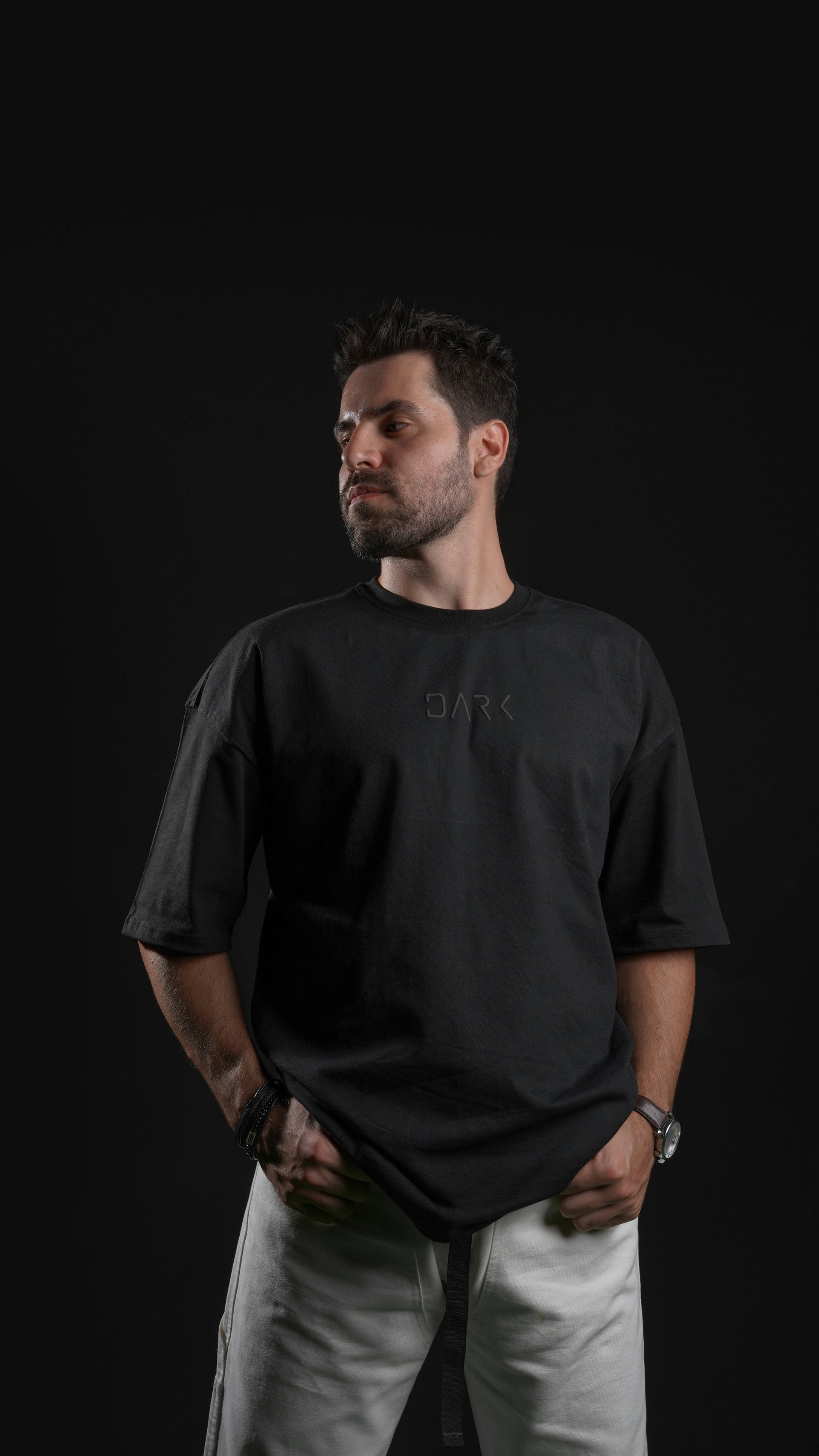 Hombre con camiseta negra con logo y pantalones claros.