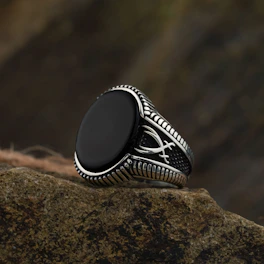 A silver ring with a black stone rests on rock.