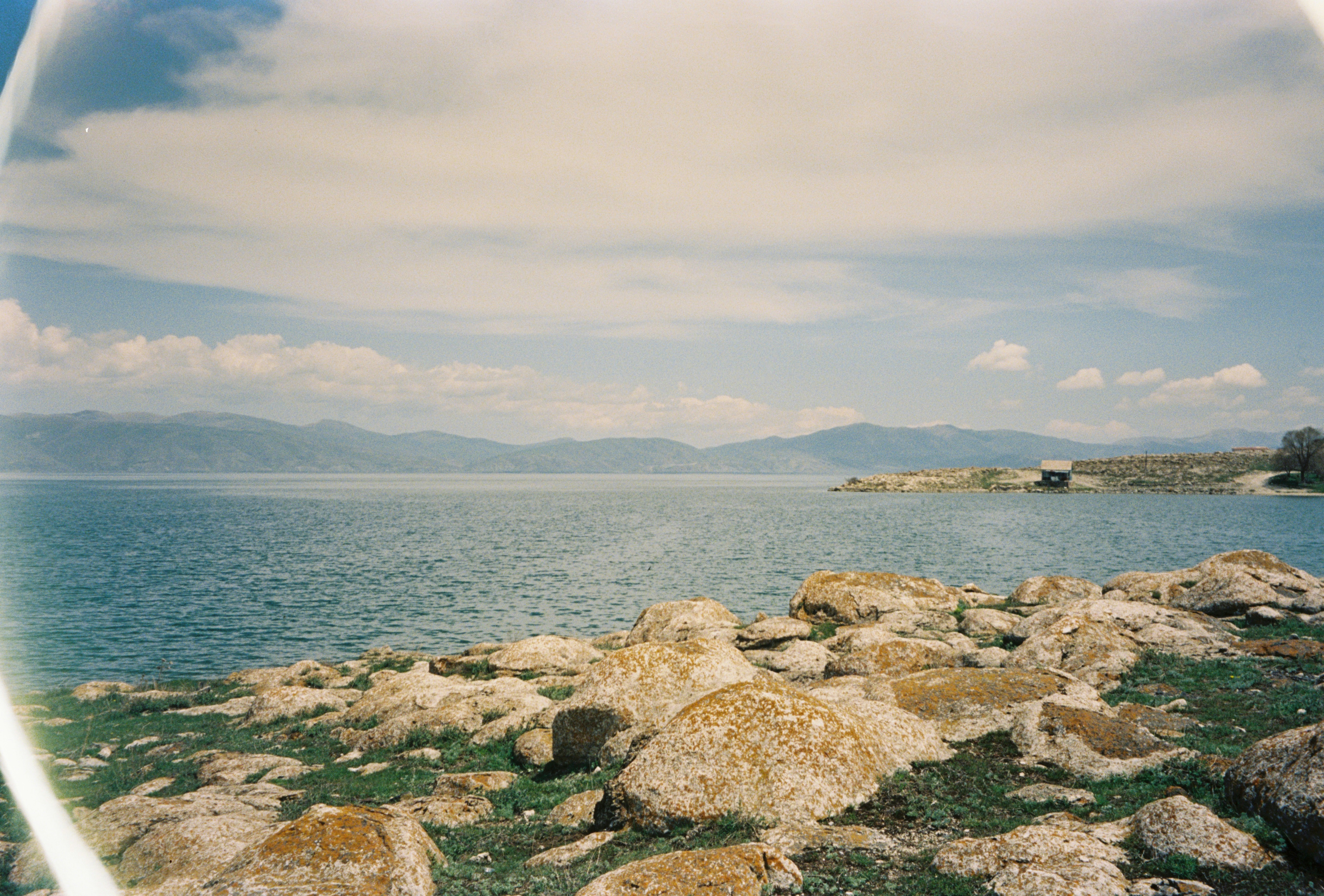 Rivage rocheux surplombant un vaste lac bleu et des montagnes lointaines.