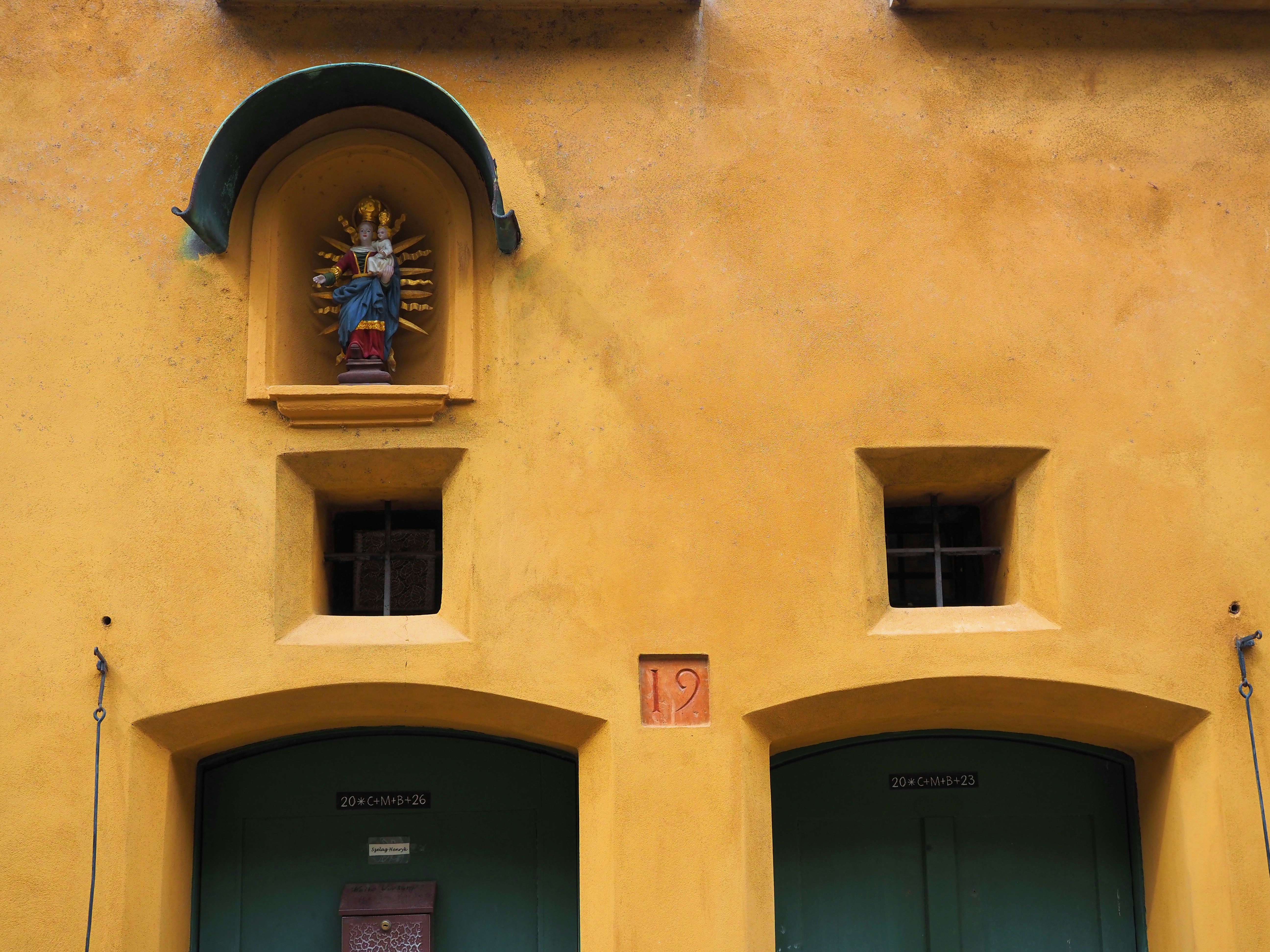A statue above two arched doorways on a yellow wall.