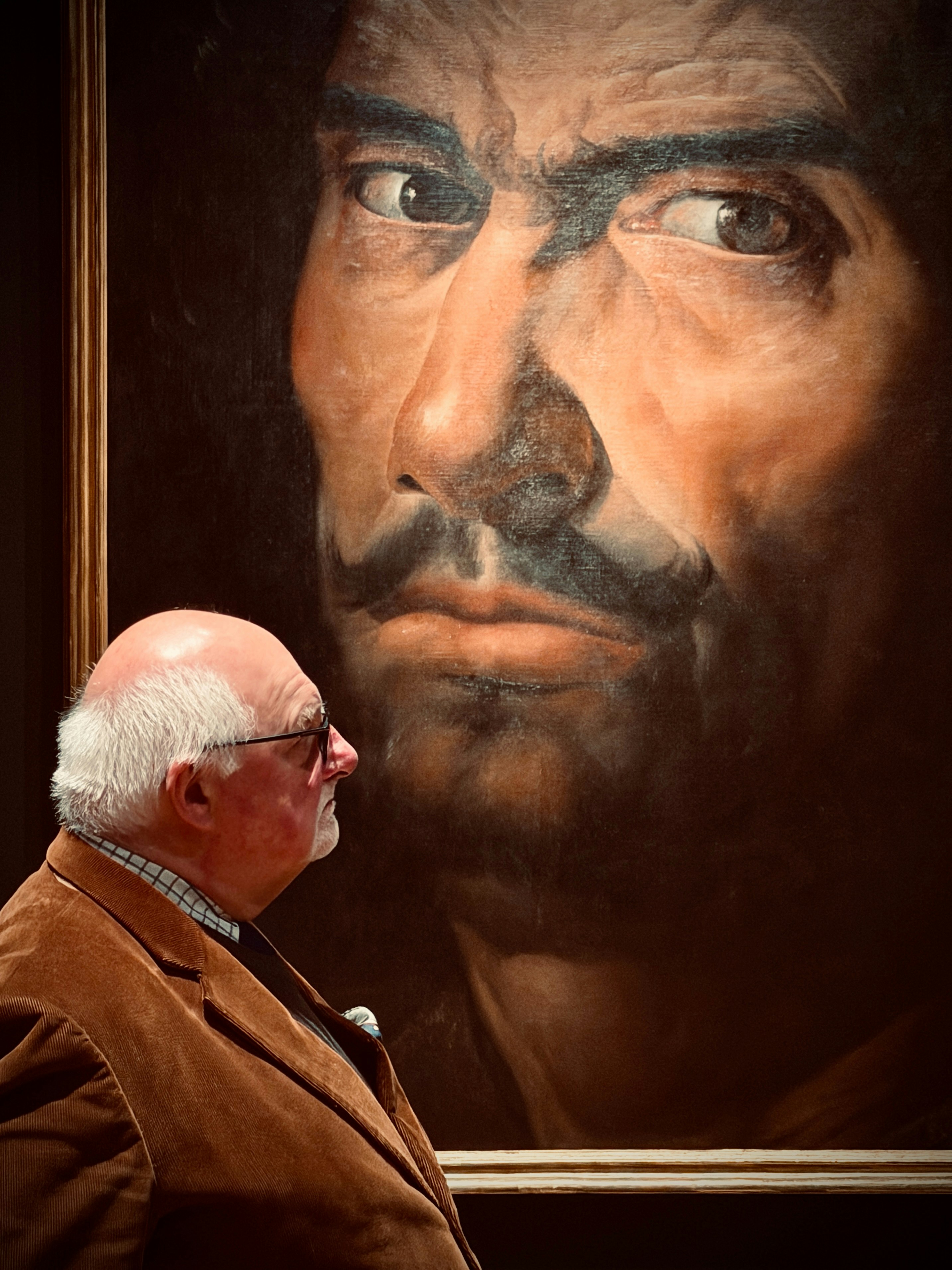 Homem olha para uma grande pintura dramática de um rosto.