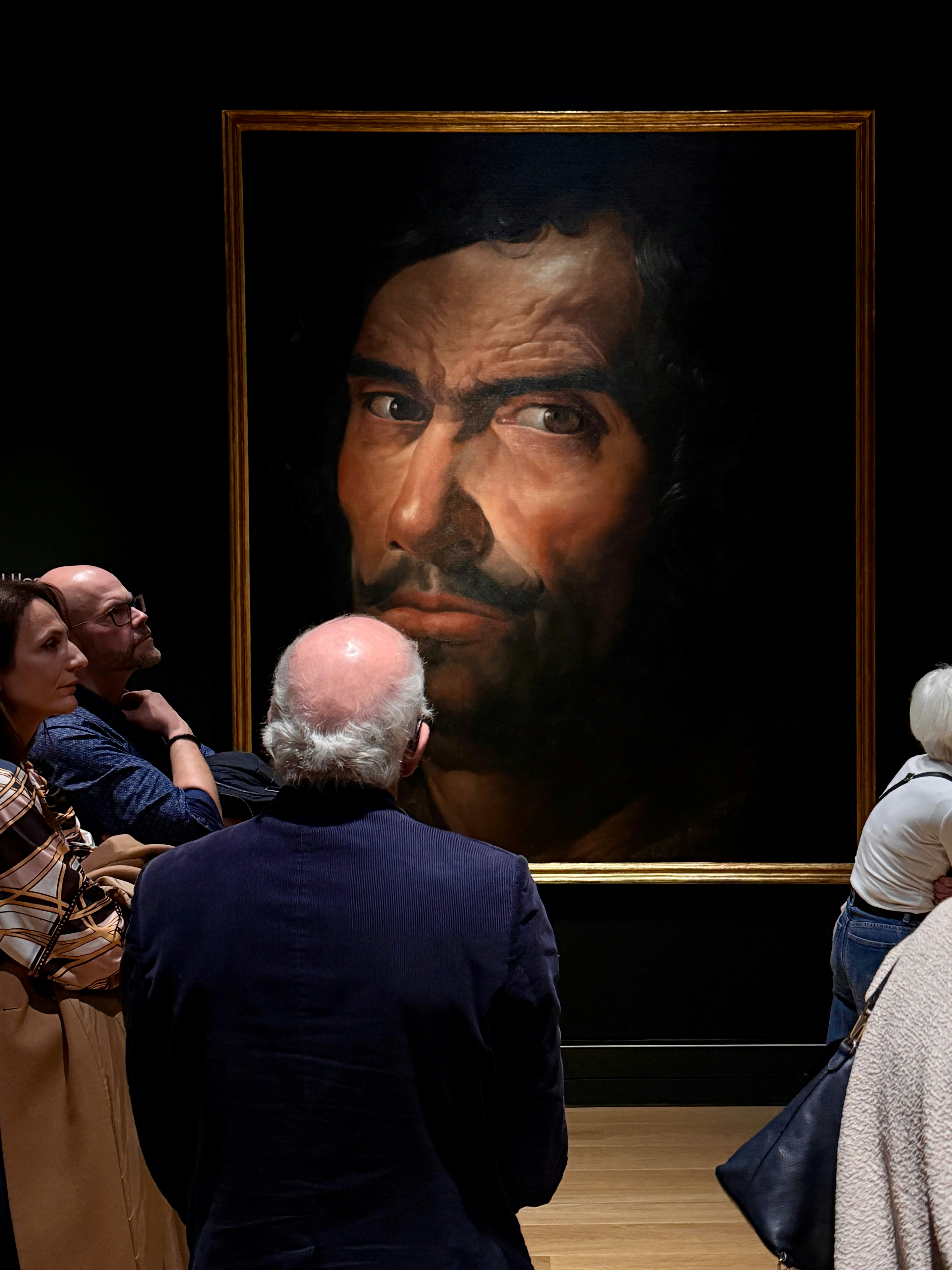 As pessoas admiram um grande retrato dramático em um museu.