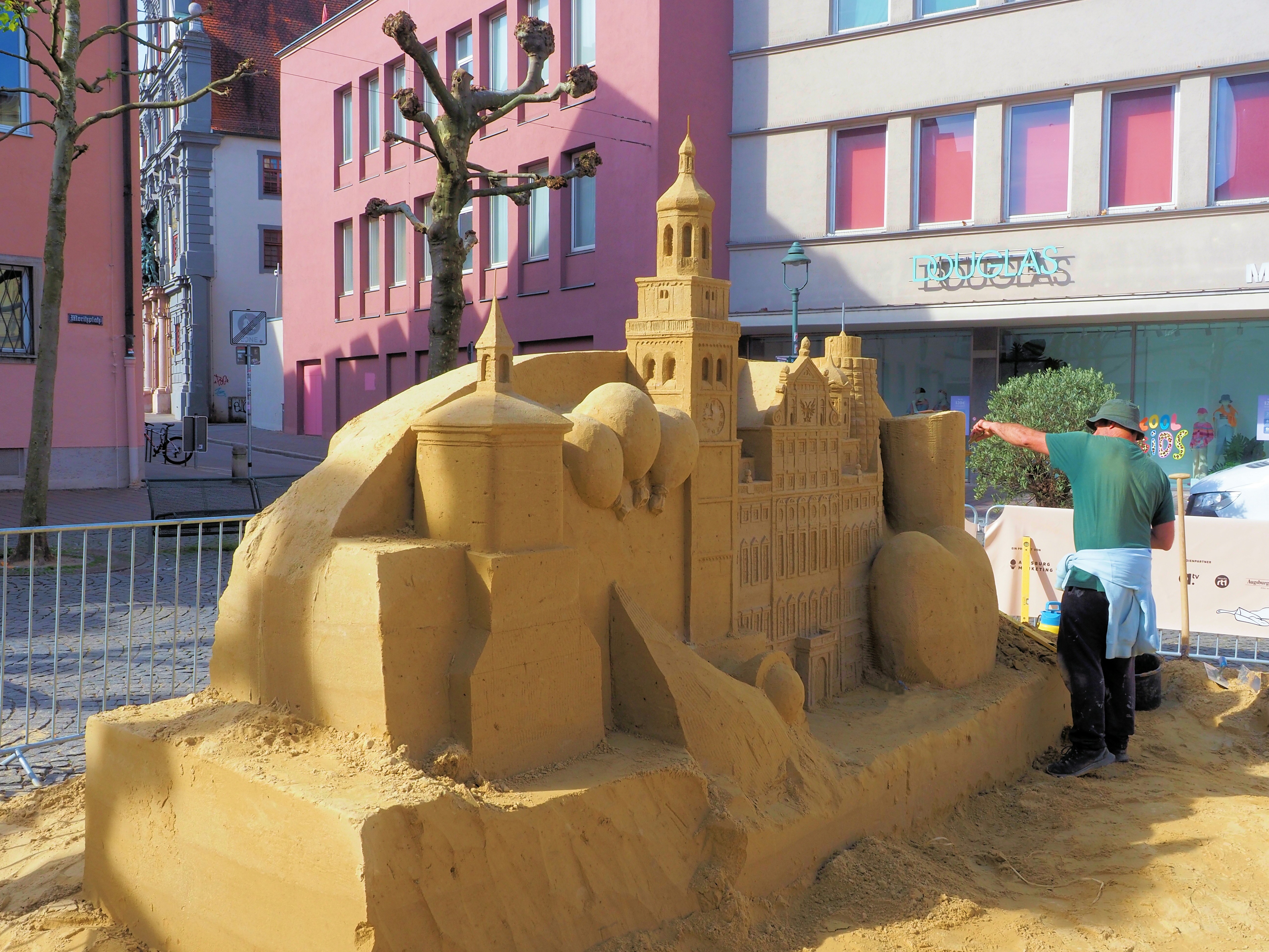 A person creates a detailed sandcastle sculpture of buildings.