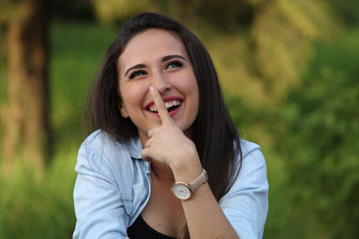 A young woman playfully touching her nose outdoors.