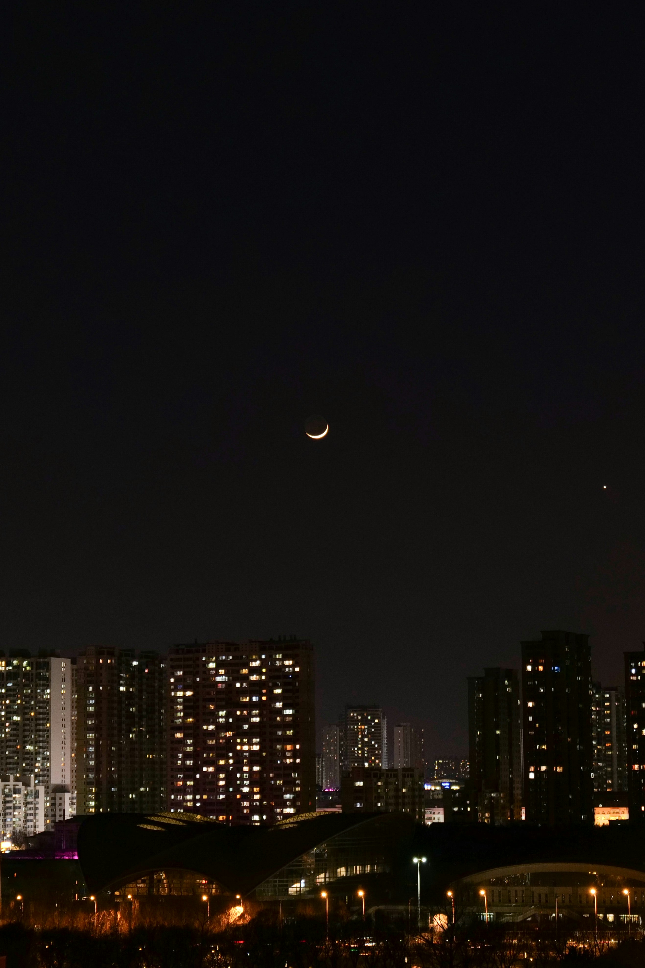 Crescent moon over illuminated city buildings at night
