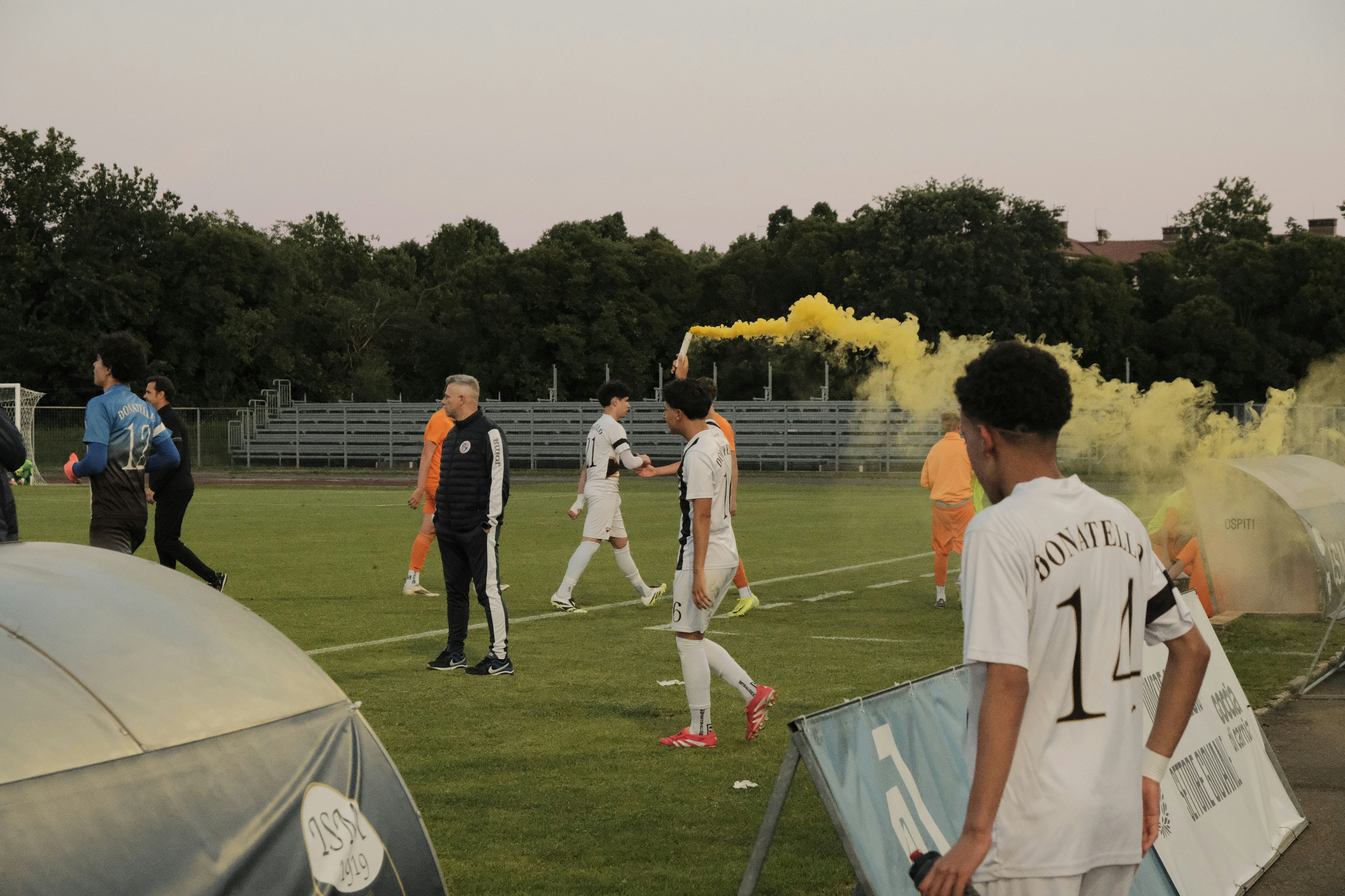 Soccer players on field with yellow smoke flare.