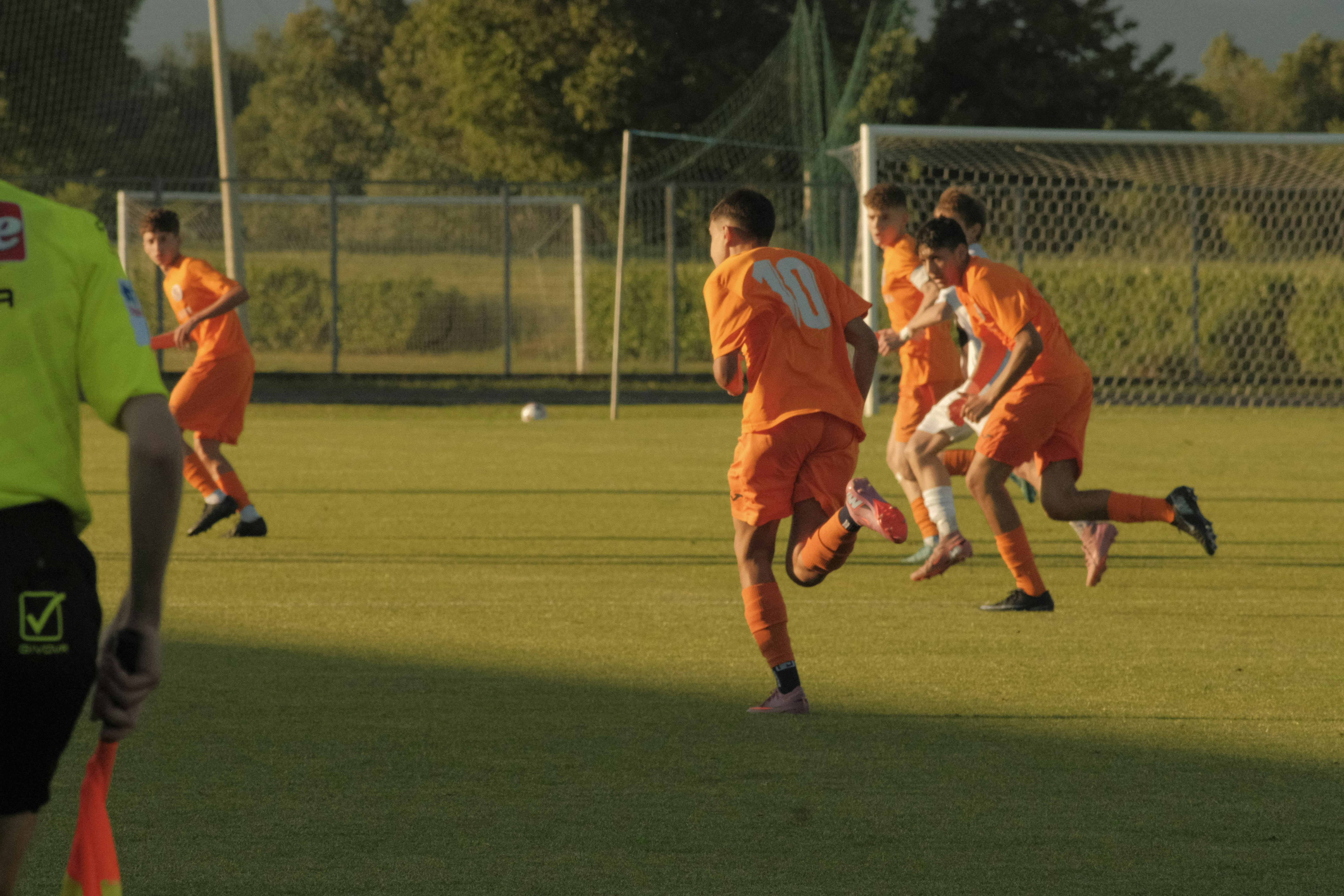 Soccer players in orange jerseys running on a green field.
