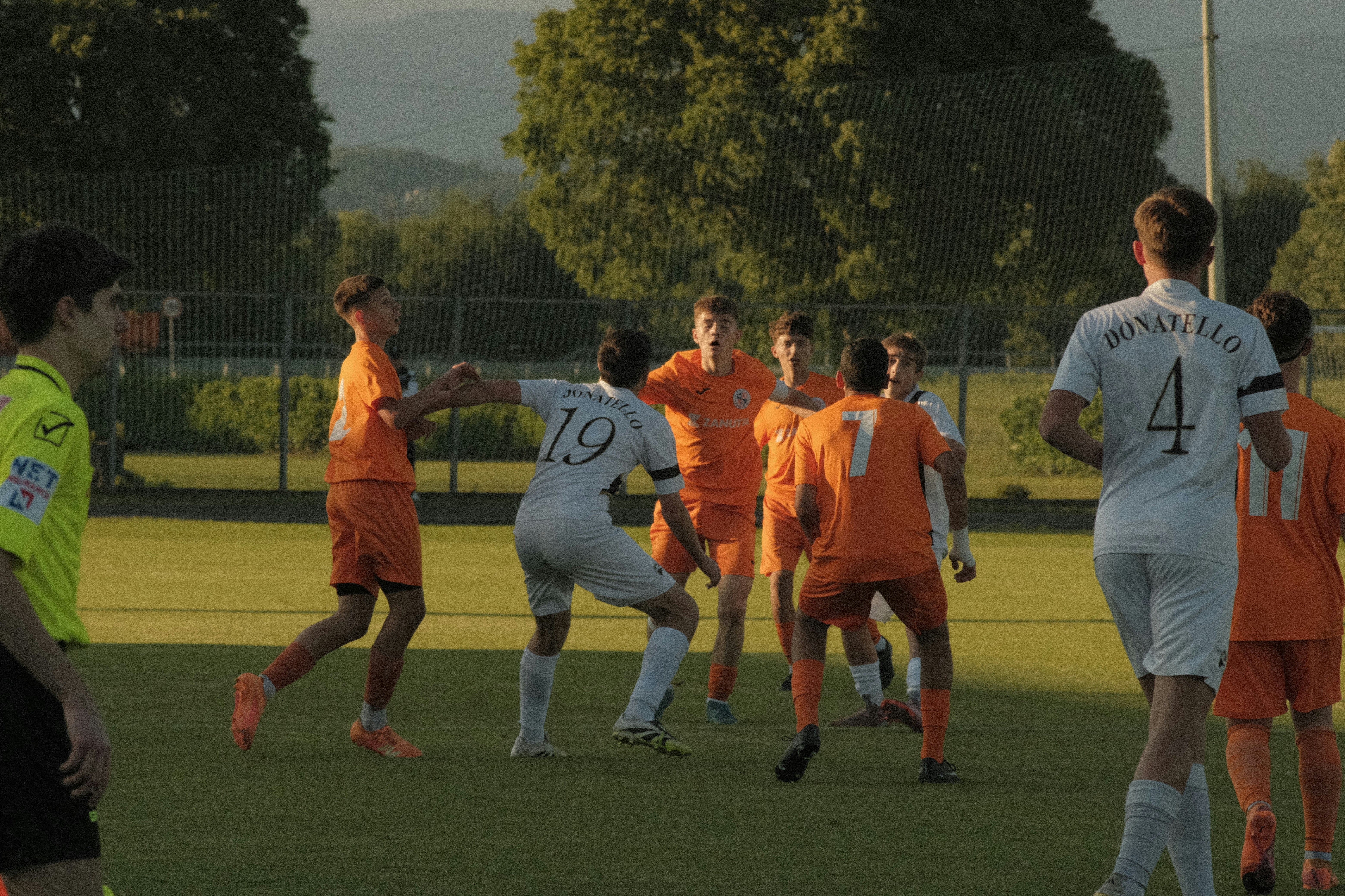 Young soccer players in orange and white uniforms on field.