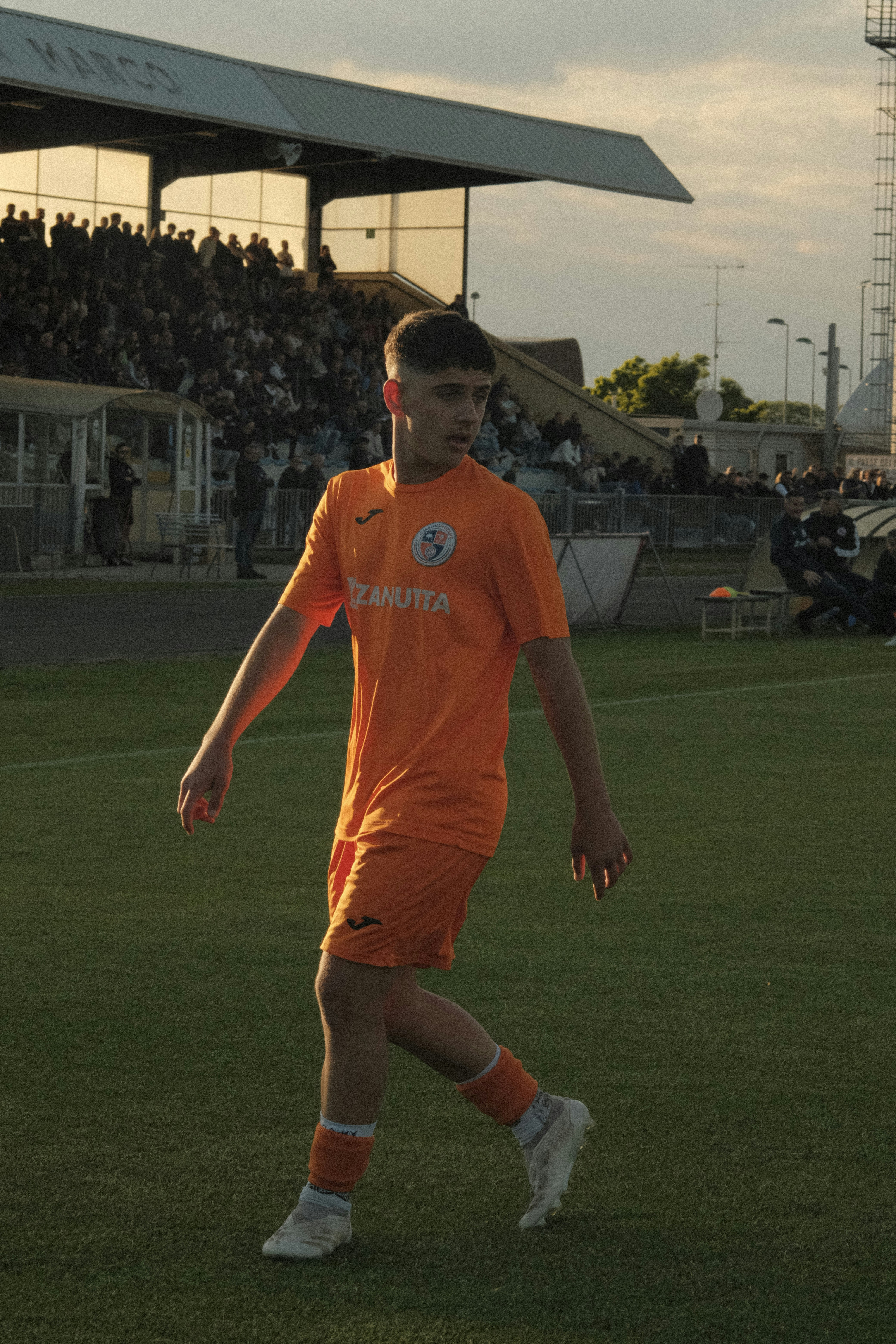 Young male soccer player in orange uniform on green field.