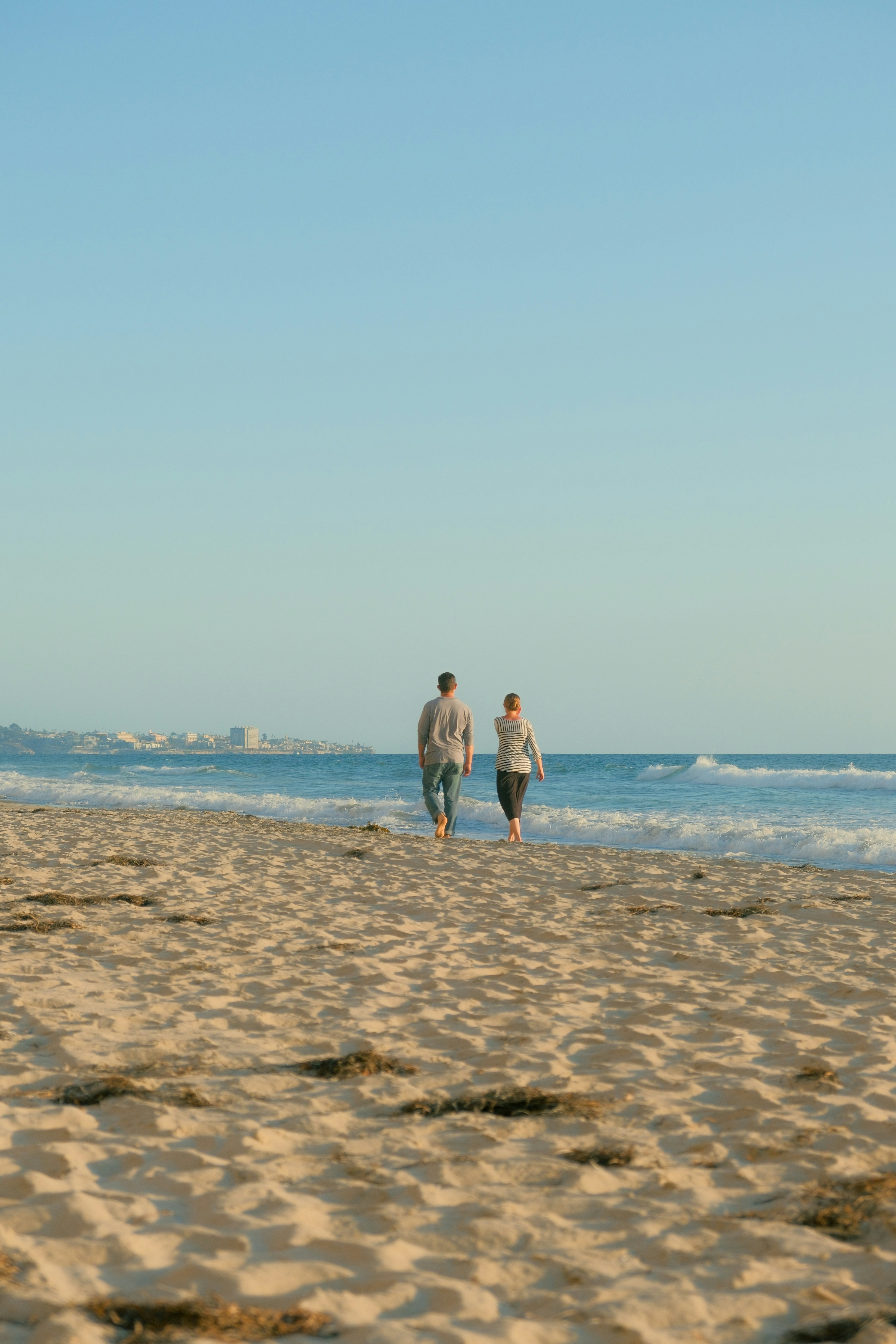 Zwei Personen gehen an einem Sandstrand in Richtung Ozean.