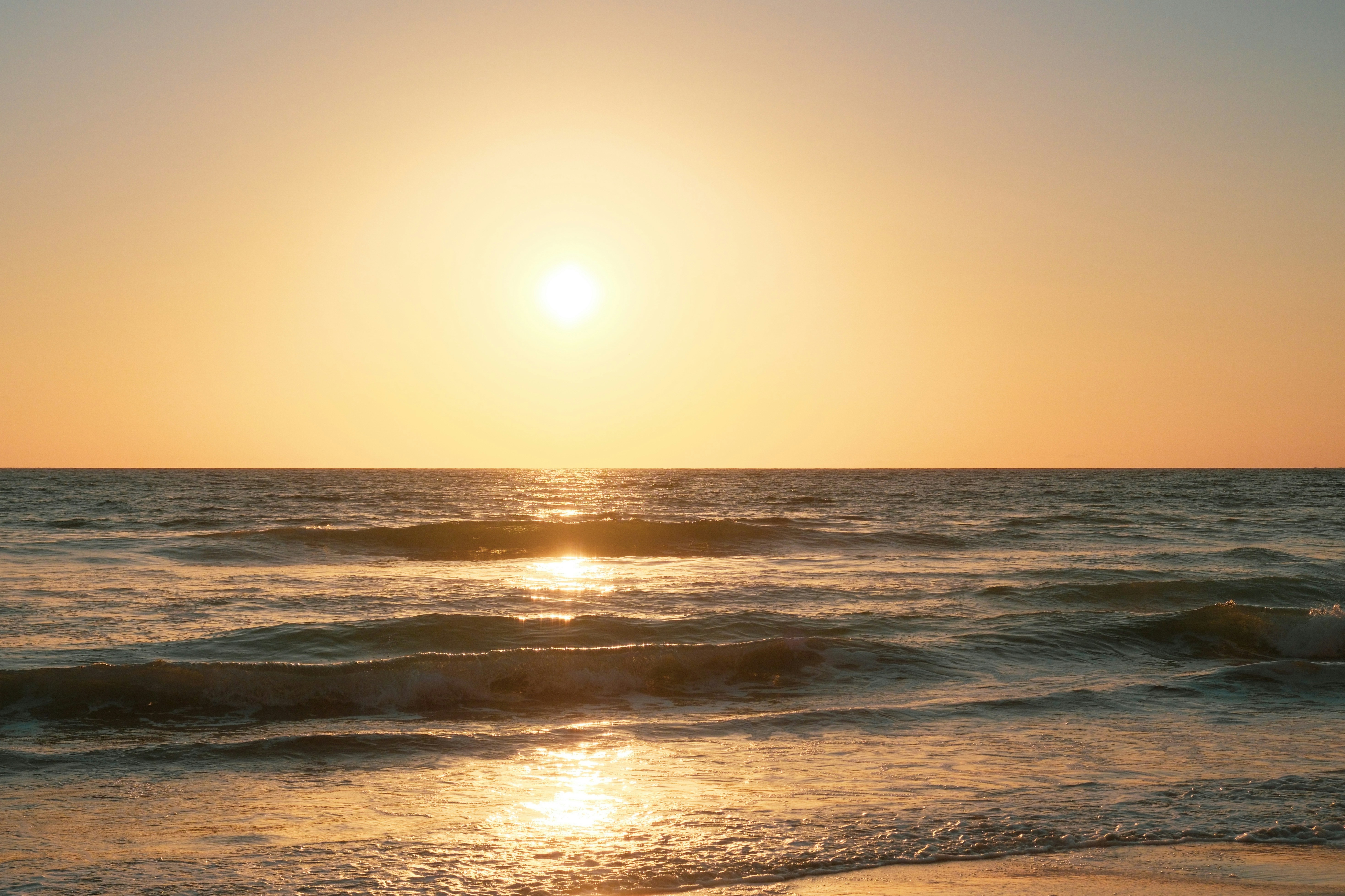 Goldener Sonnenuntergang über einem ruhigen Ozean mit sanften Wellen.