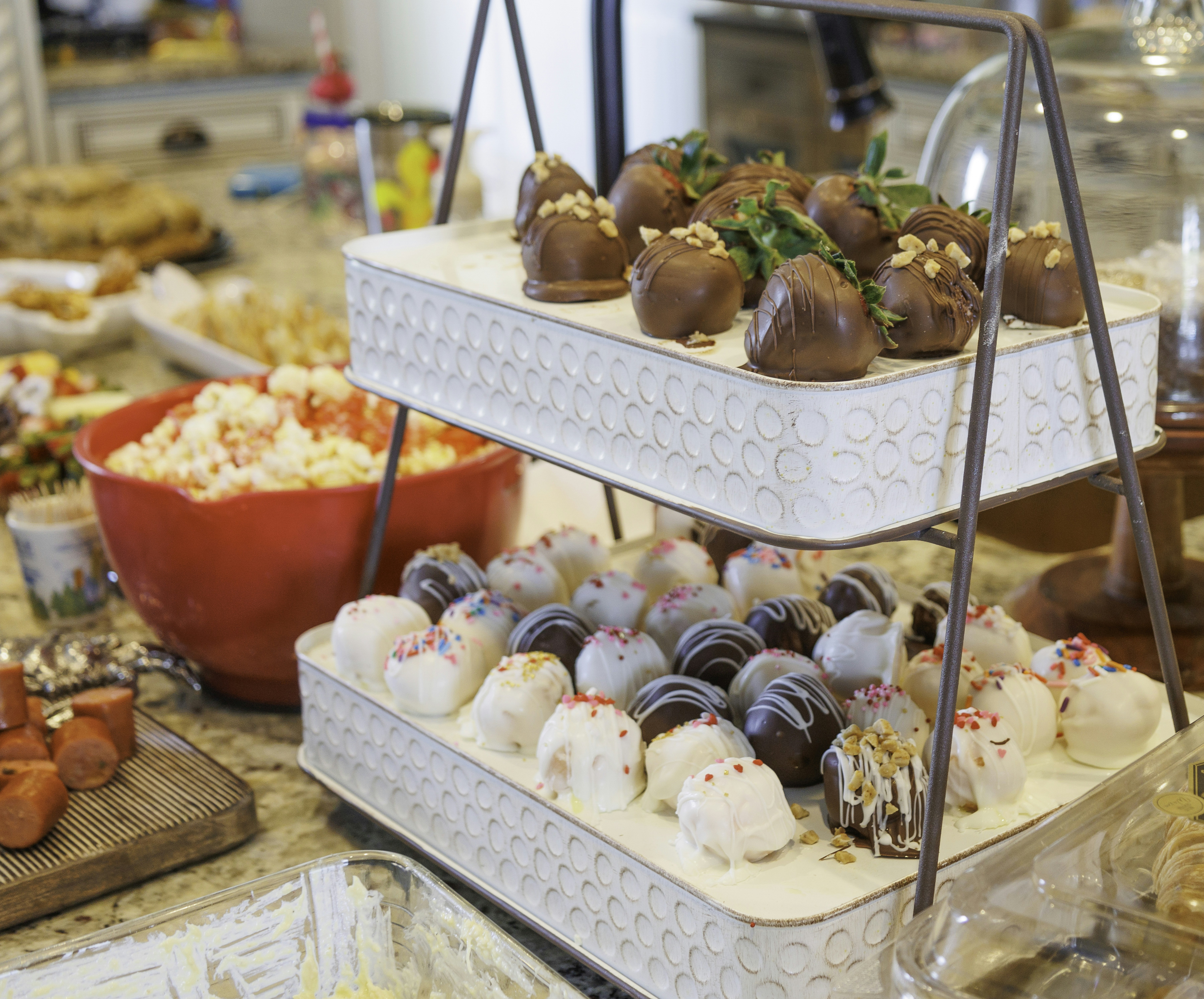 A tiered container holds desserts like chocolate covered strawberries.