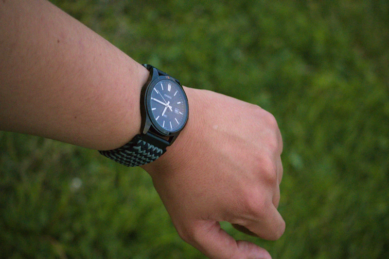 Arm wearing a black watch over green grass