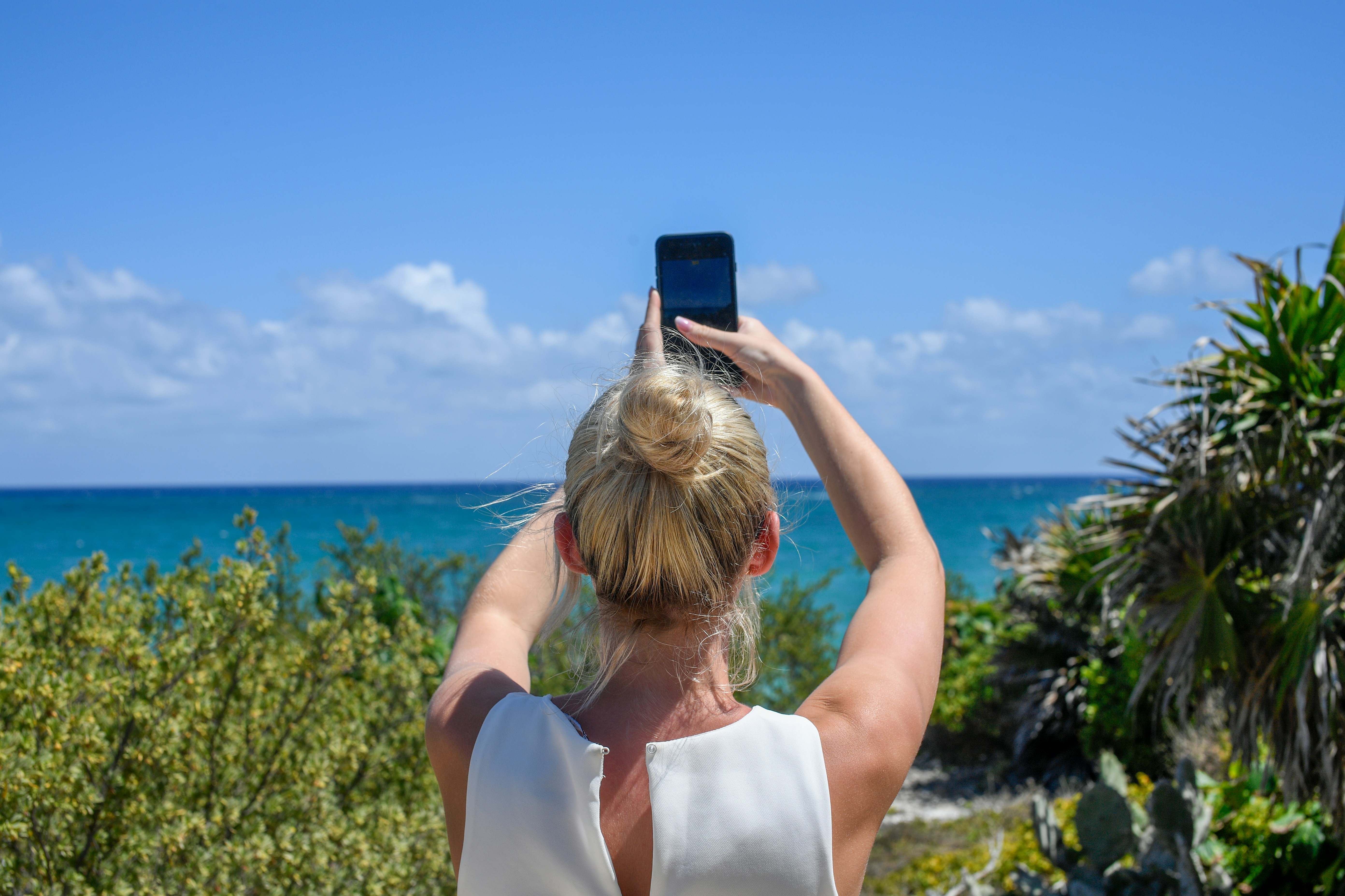 Woman taking a picture of the ocean with her phone.