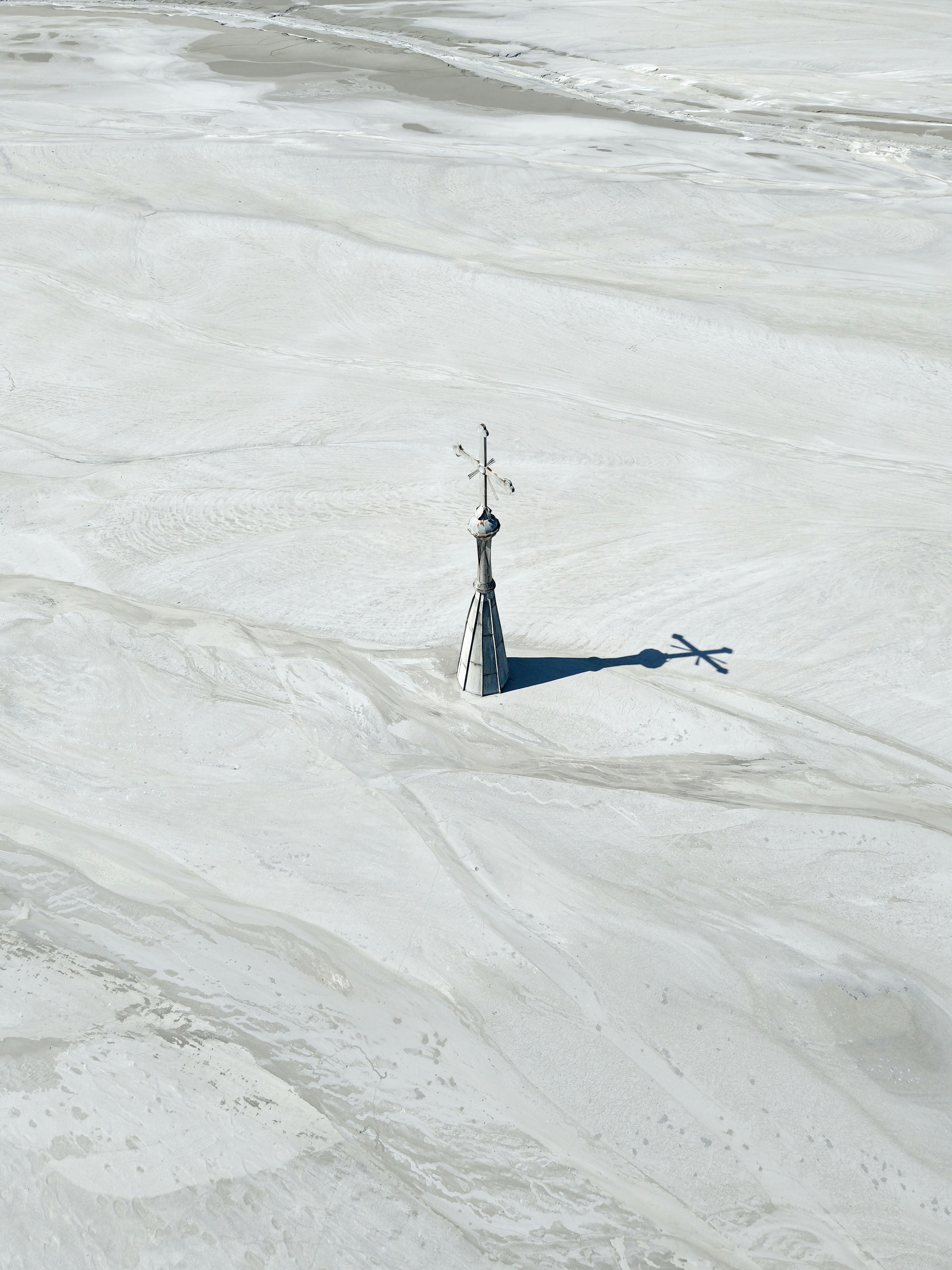 A solitary weather vane stands on a frozen lake.