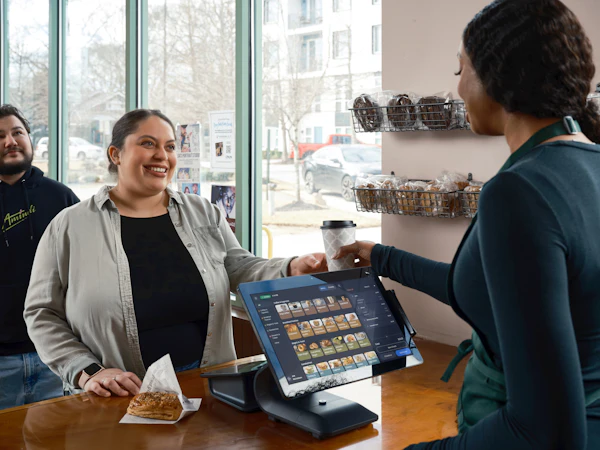 A barista handing a fresh coffee across the counter to a smiling customer
