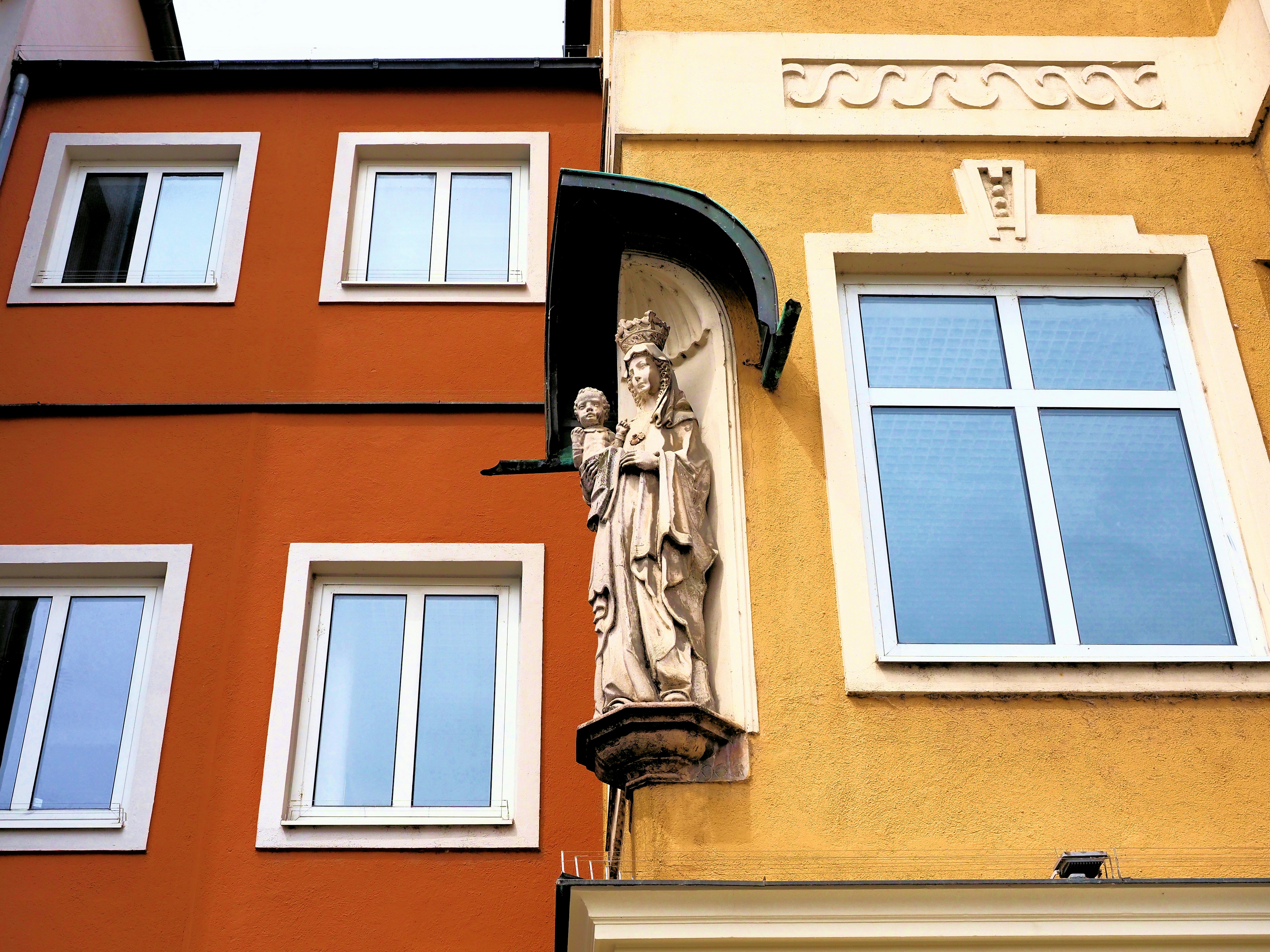 Religious statue on building corner between orange and yellow facades.