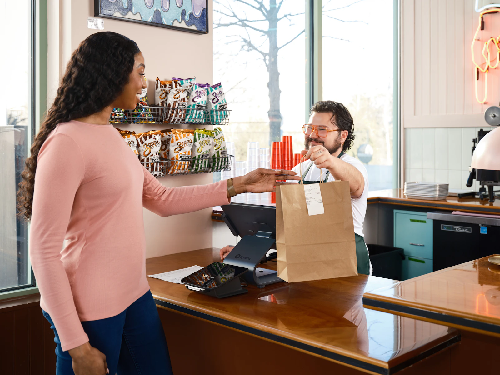 A customer collecting her order at a retail counter with a tablet register, the moment enrollment and points are recorded