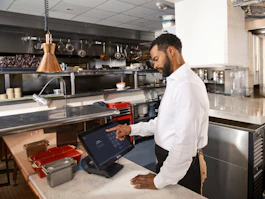 Restaurant worker uses a touch screen in a professional kitchen.