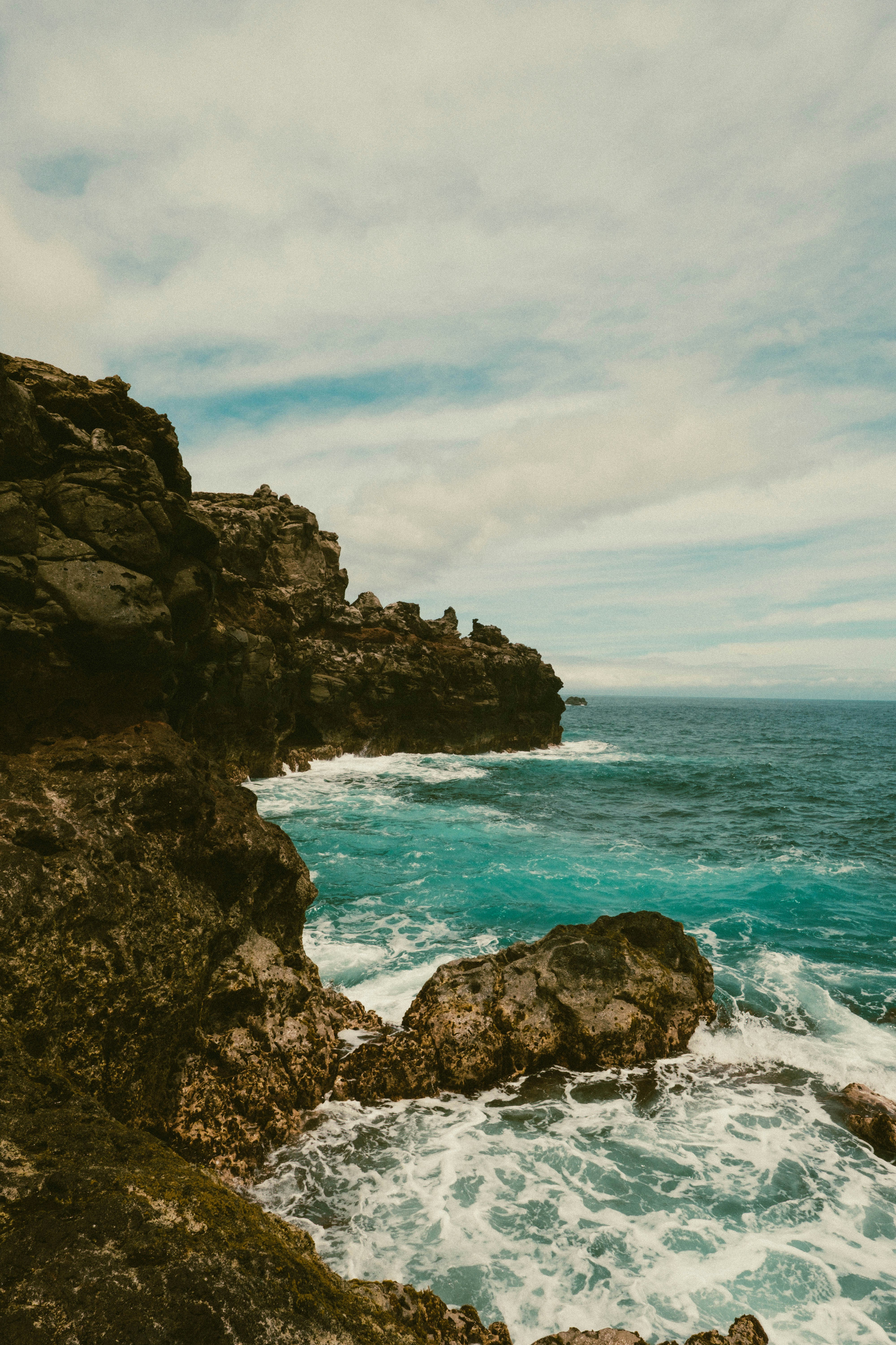 Waves crash against rocky cliffs under a cloudy sky.