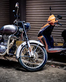 Silver motorcycle and orange scooter parked outside.