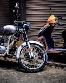 Silver motorcycle and orange scooter parked outside.