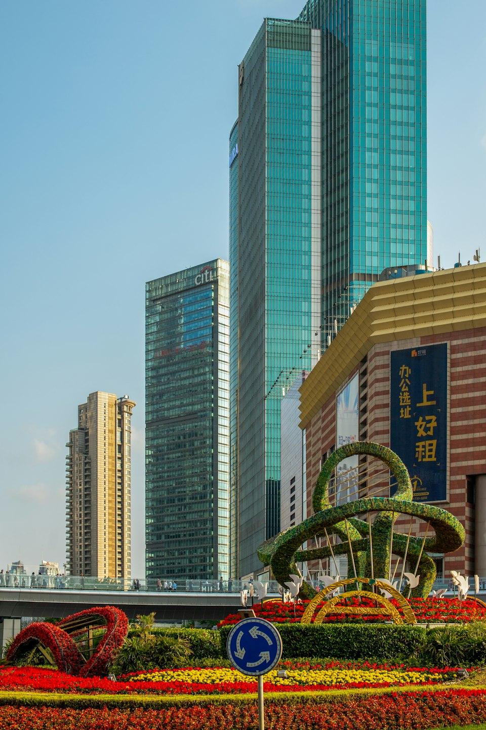 Colorful flower beds and topiary in a riverside park beneath Lujiazui's skyscrapers