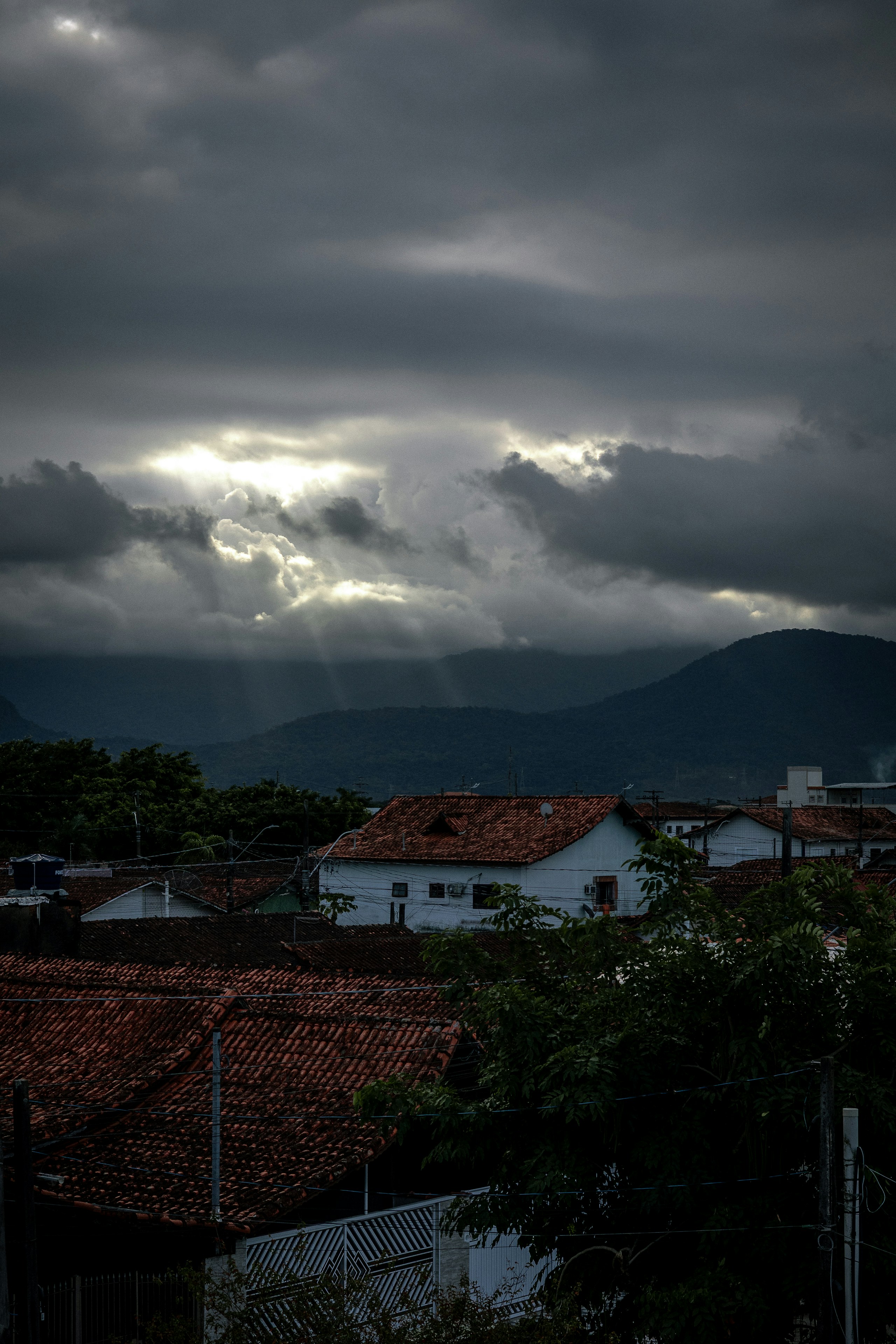 Sunlight breaks through dark clouds over houses and mountains.