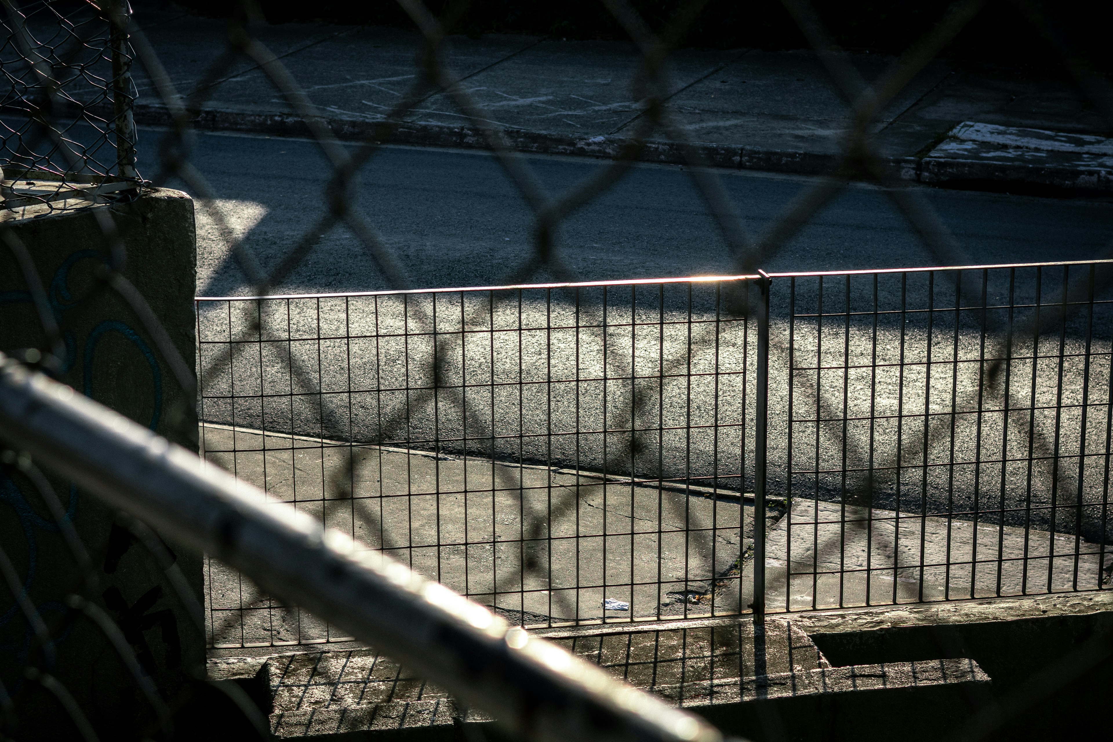 Chain-link fence casts shadows on a road.