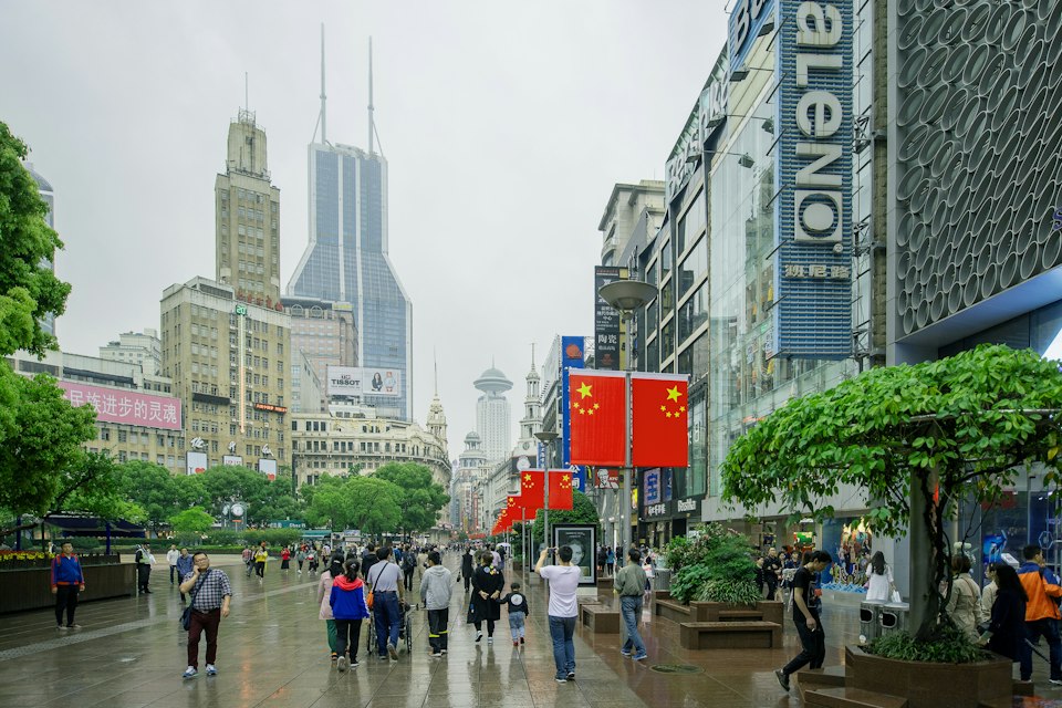 Pedestrians walking along the bustling East Nanjing Road shopping street decorated with flags