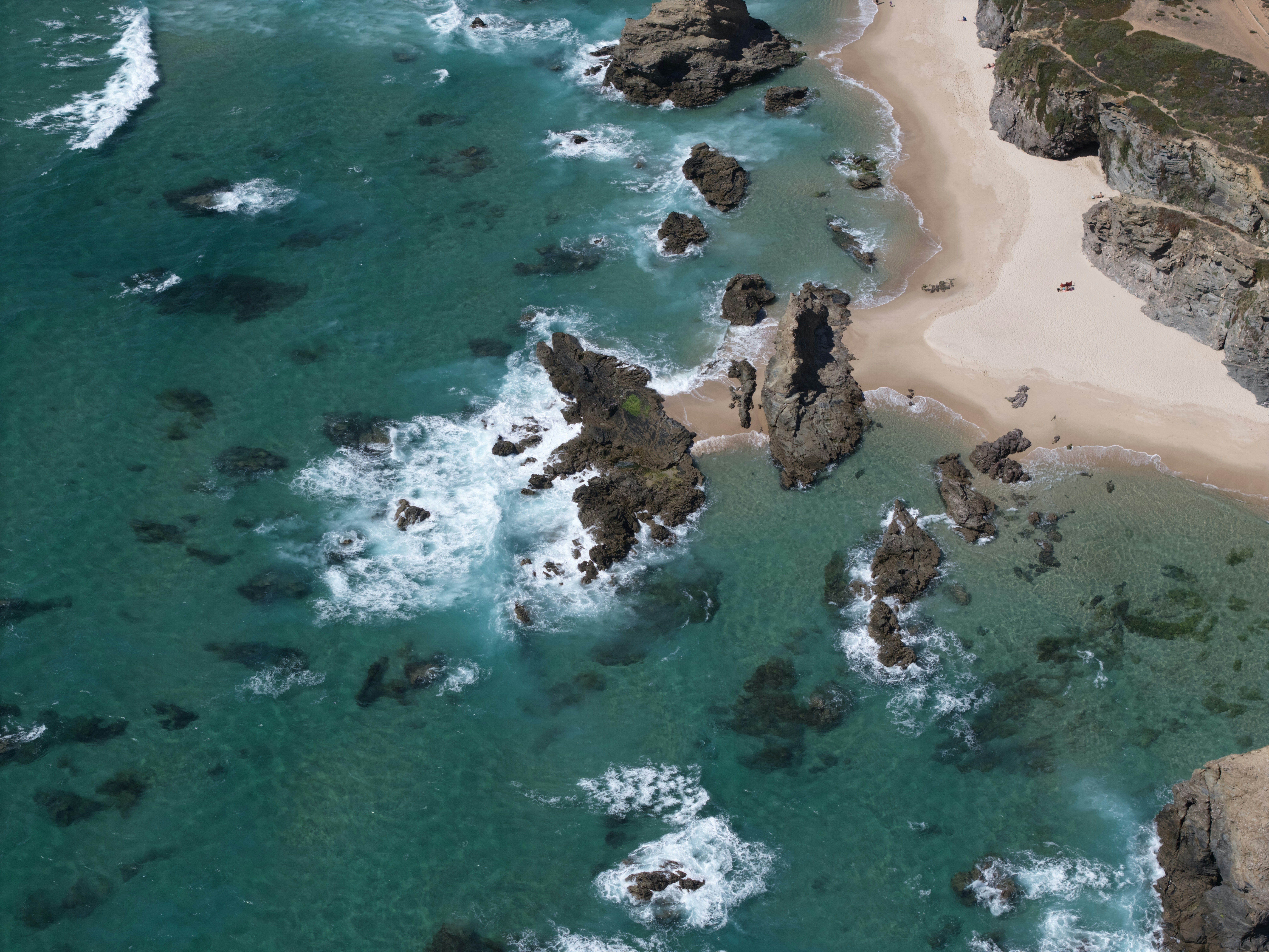 Turquoise ocean waves crash on rocky shore and sandy coastline.