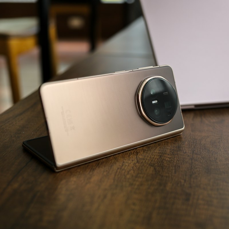 Book-style foldable smartphone with a large circular rear camera module, resting open on a wooden table