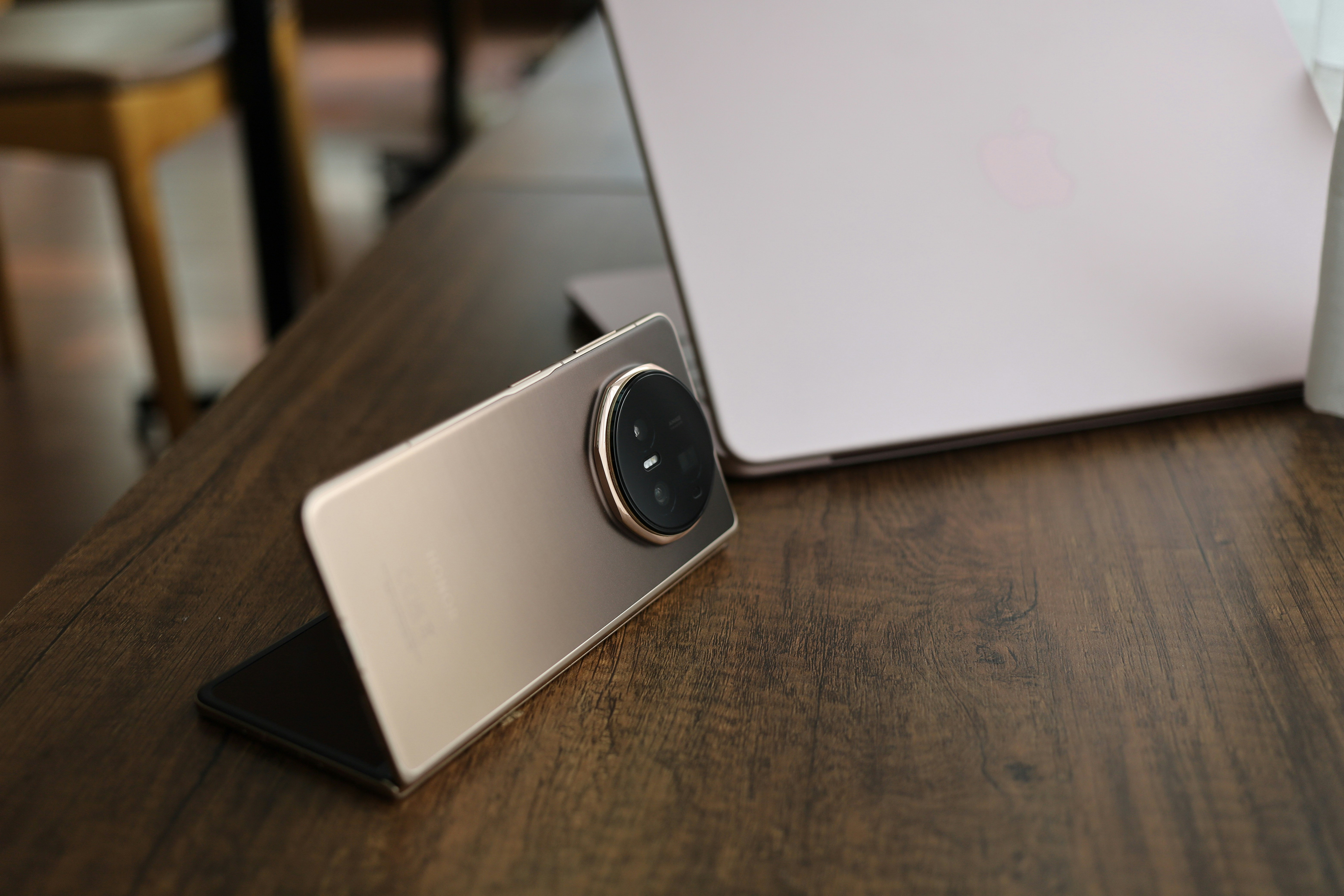 Modern foldable phone on a wooden table with laptop.