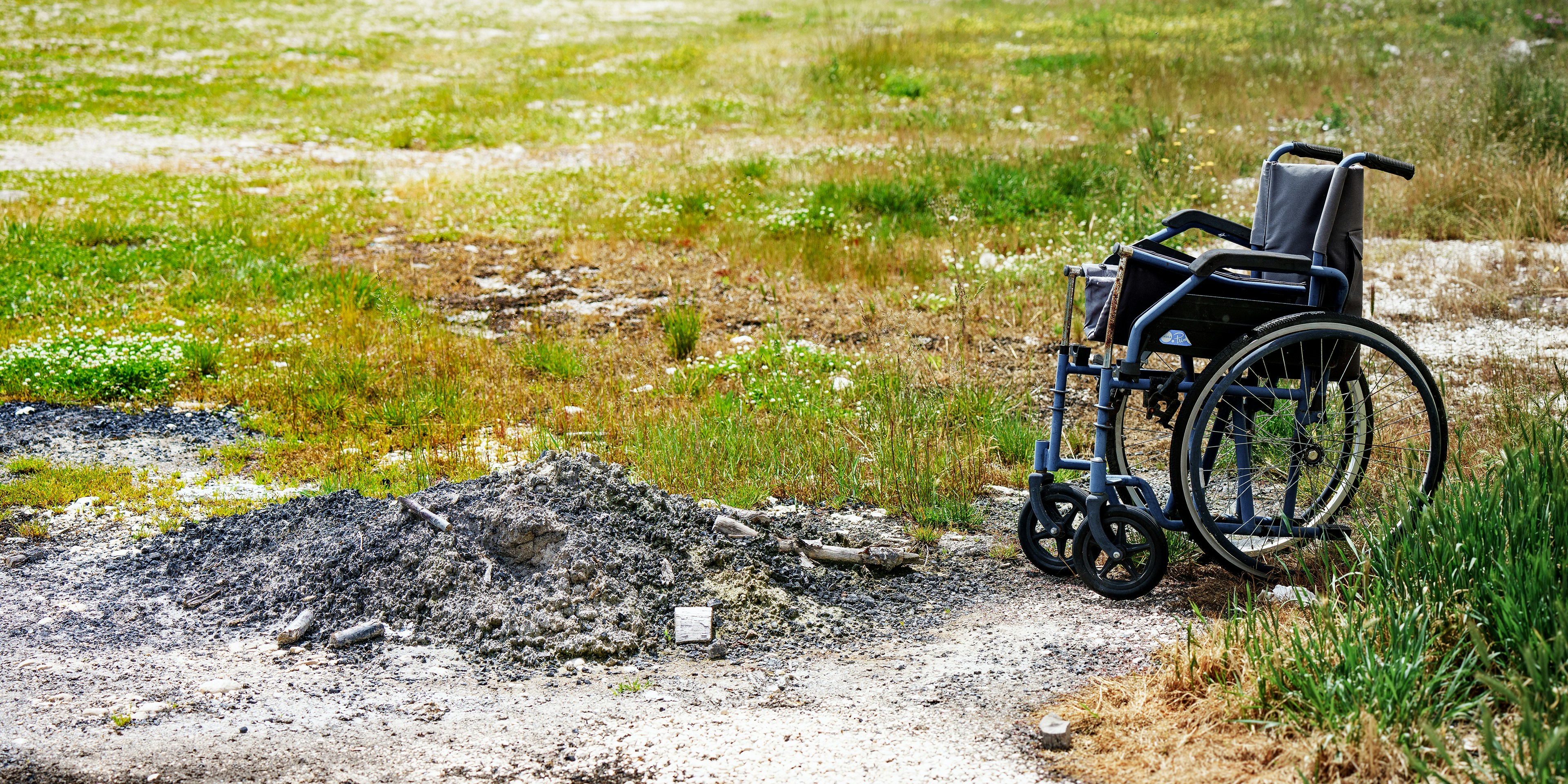 A wheelchair sits abandoned in a grassy, overgrown area.