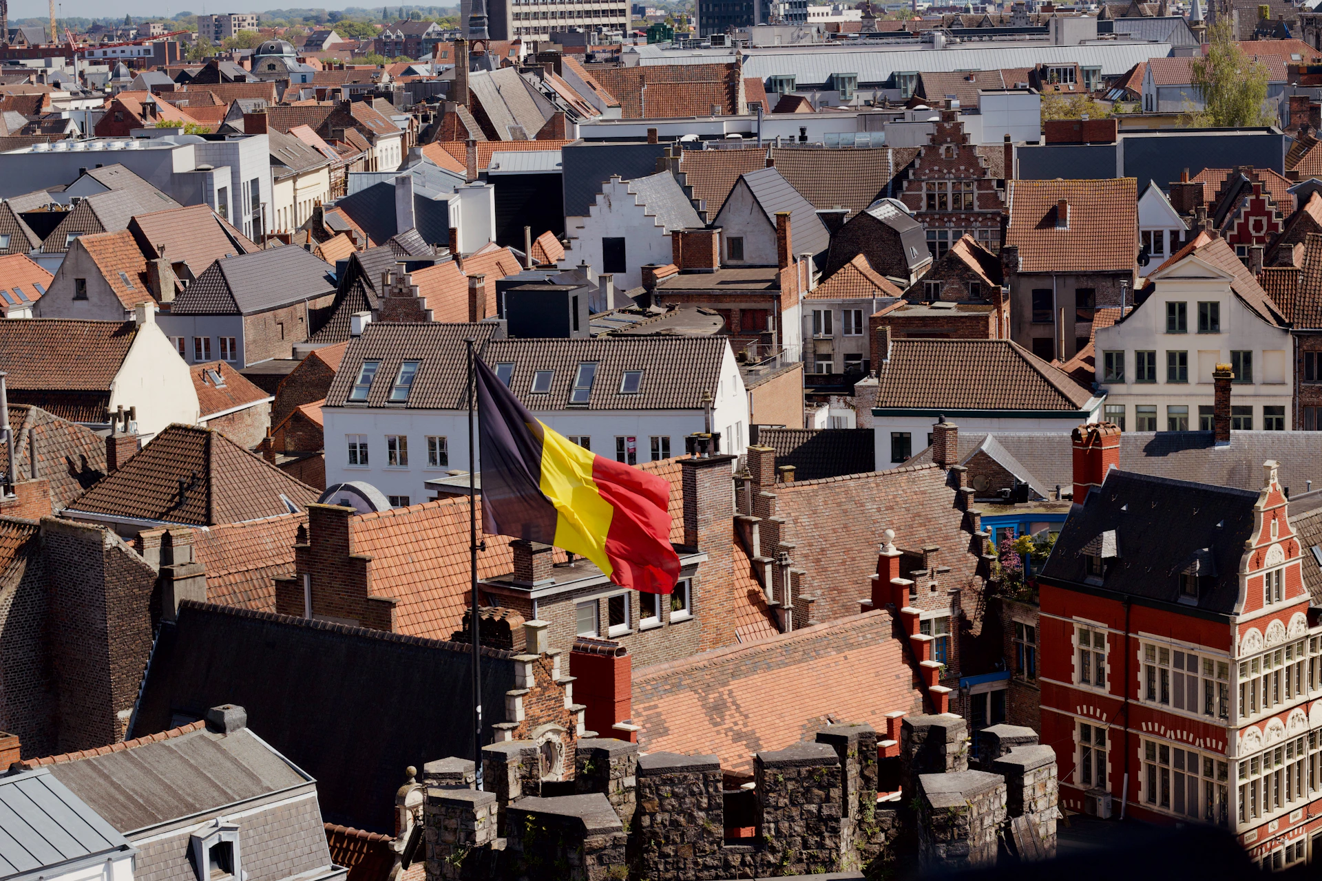 Belgian flag flying over a city with many red-tiled roofs