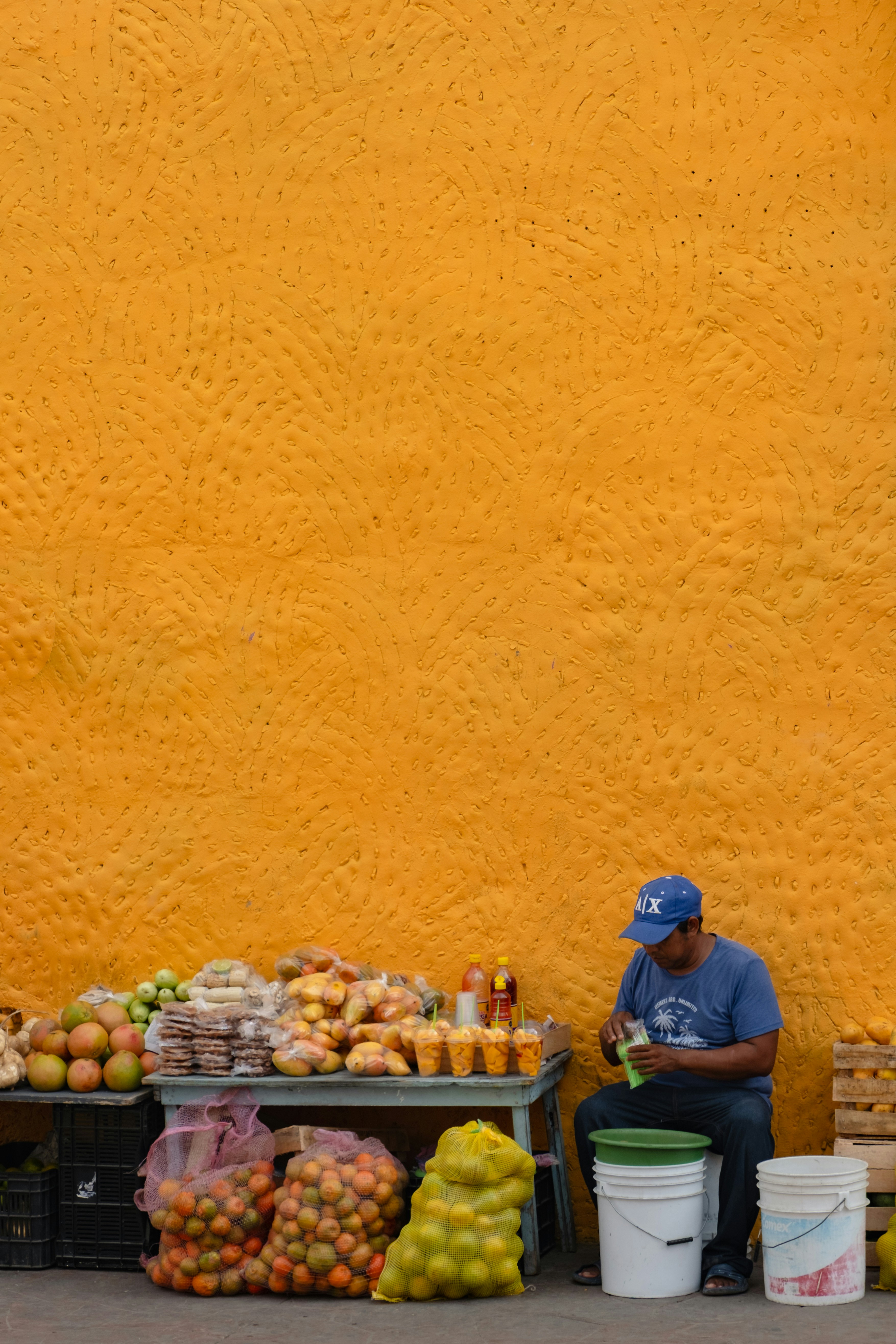 Man sitting by fruit stand against textured orange wall