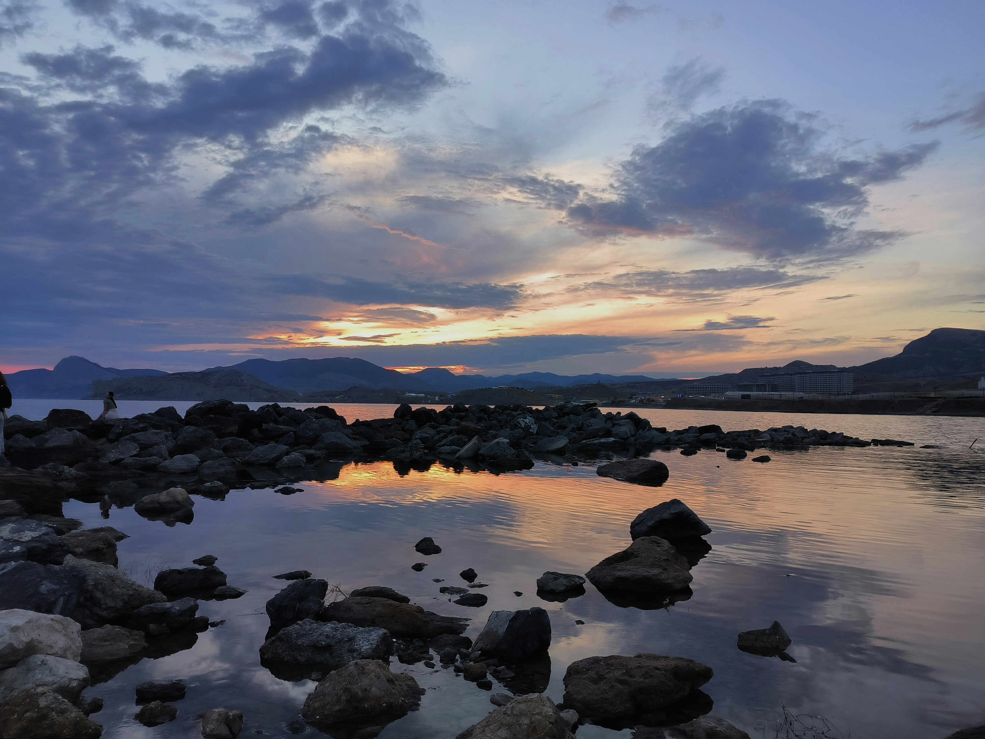 岩だらけの岸辺に、夕焼けの空を映す穏やかな水面。