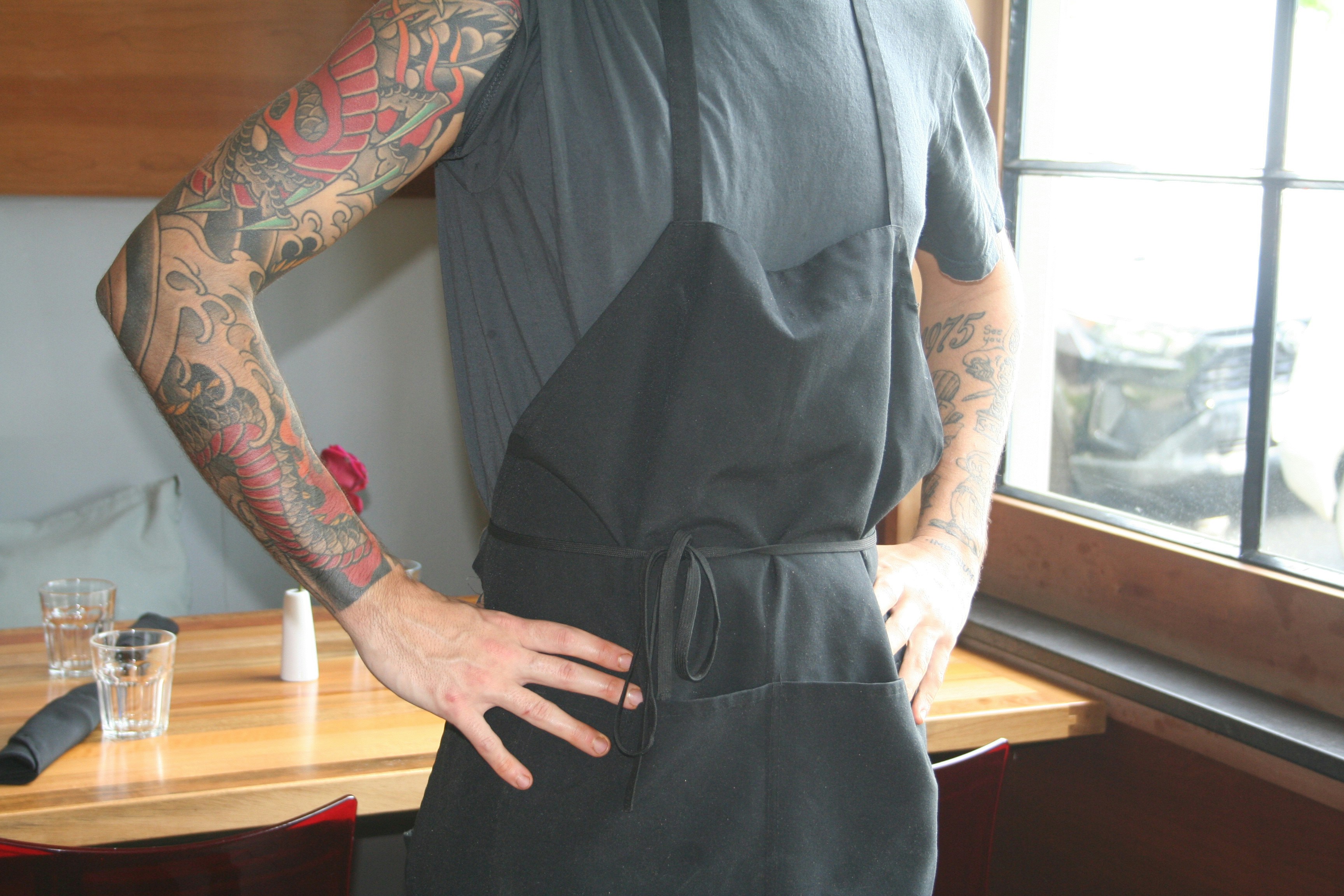 Person with tattoos wearing a black apron