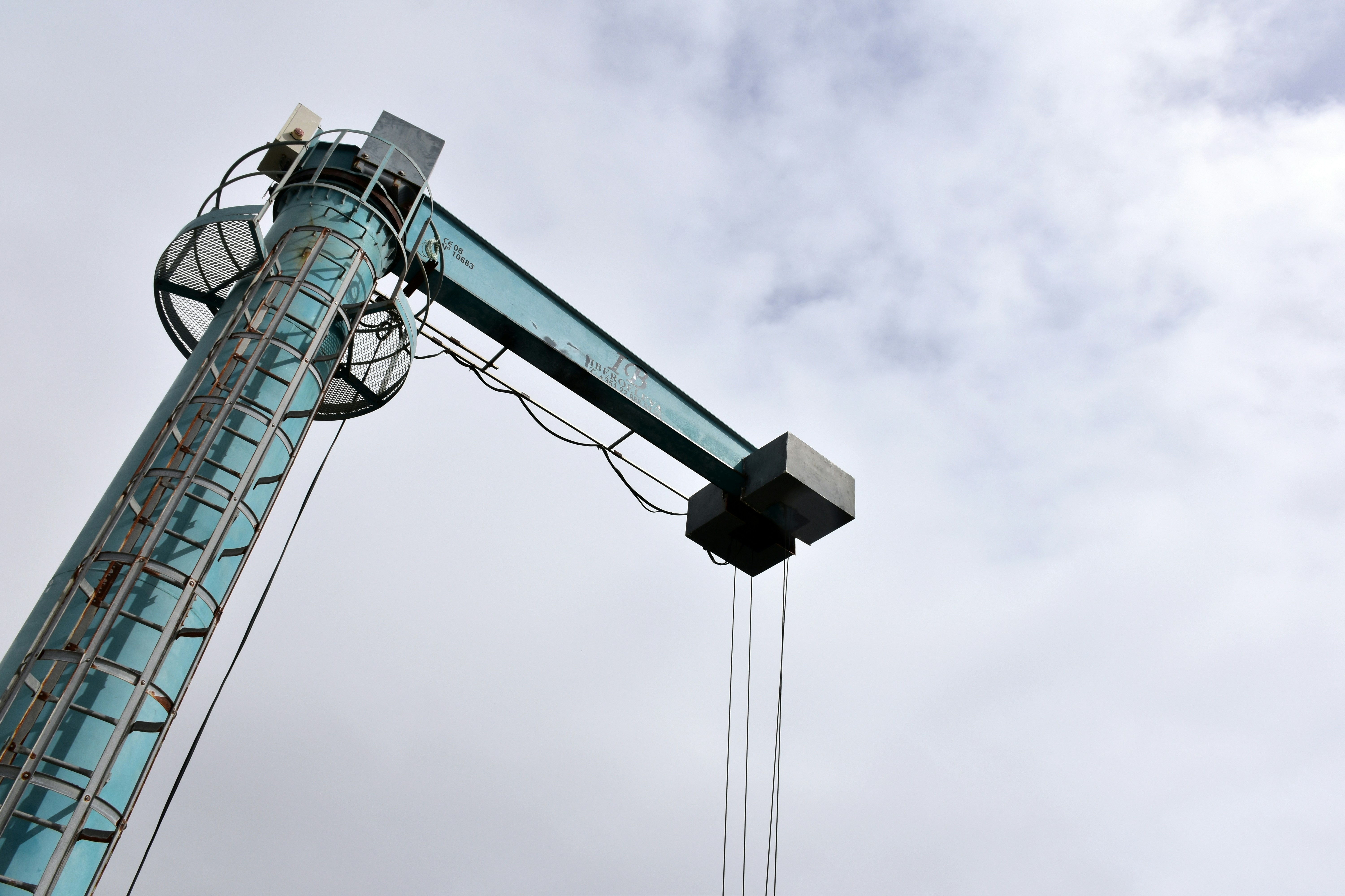Tall industrial tower with a crane arm against cloudy sky