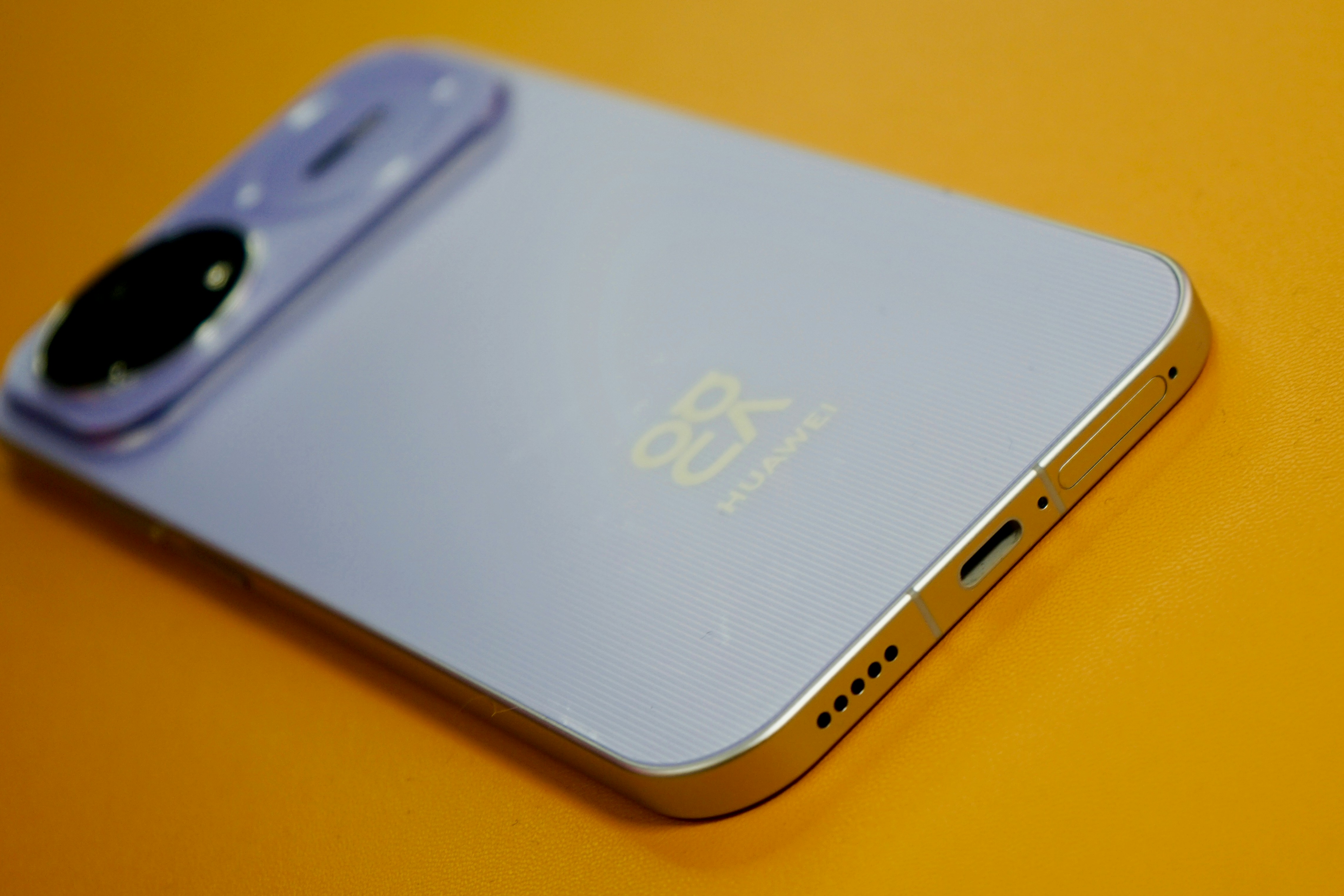 Smartphone violet clair avec appareil photo et logo sur fond orange.