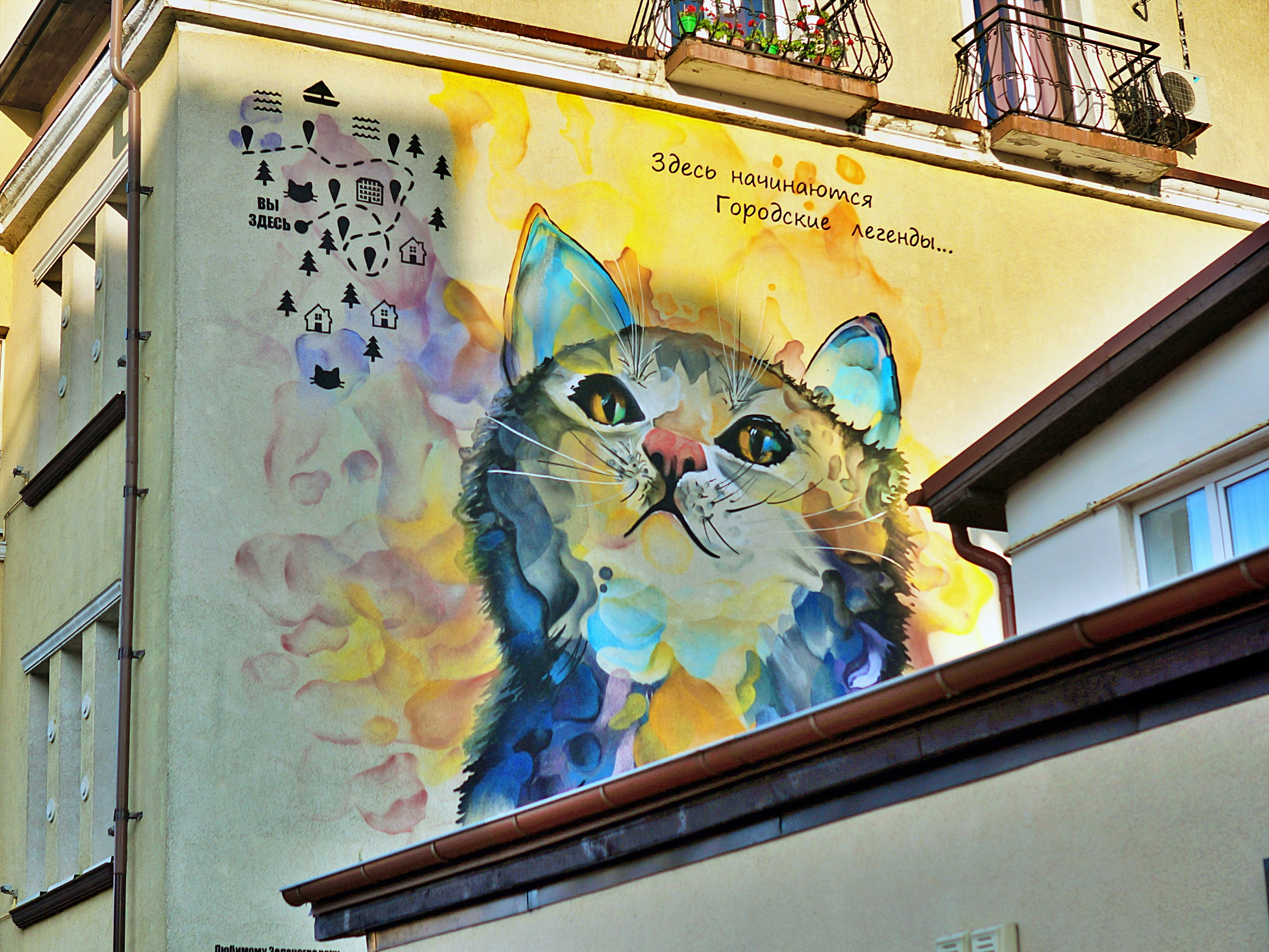 Mural kucing besar dan berwarna-warni di fasad bangunan.