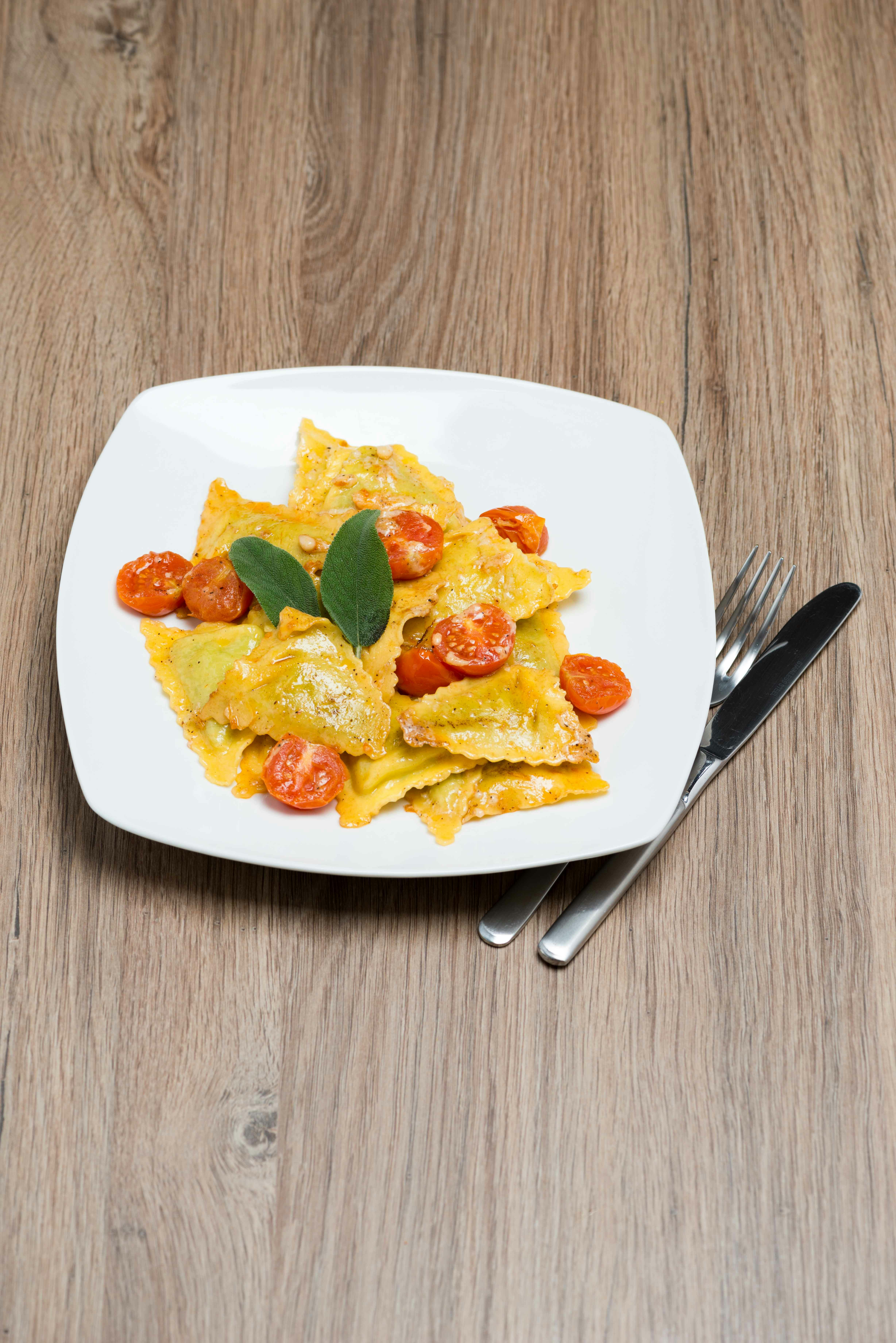 Ravioli con pomodorini ciliegia e salvia su un piatto bianco.