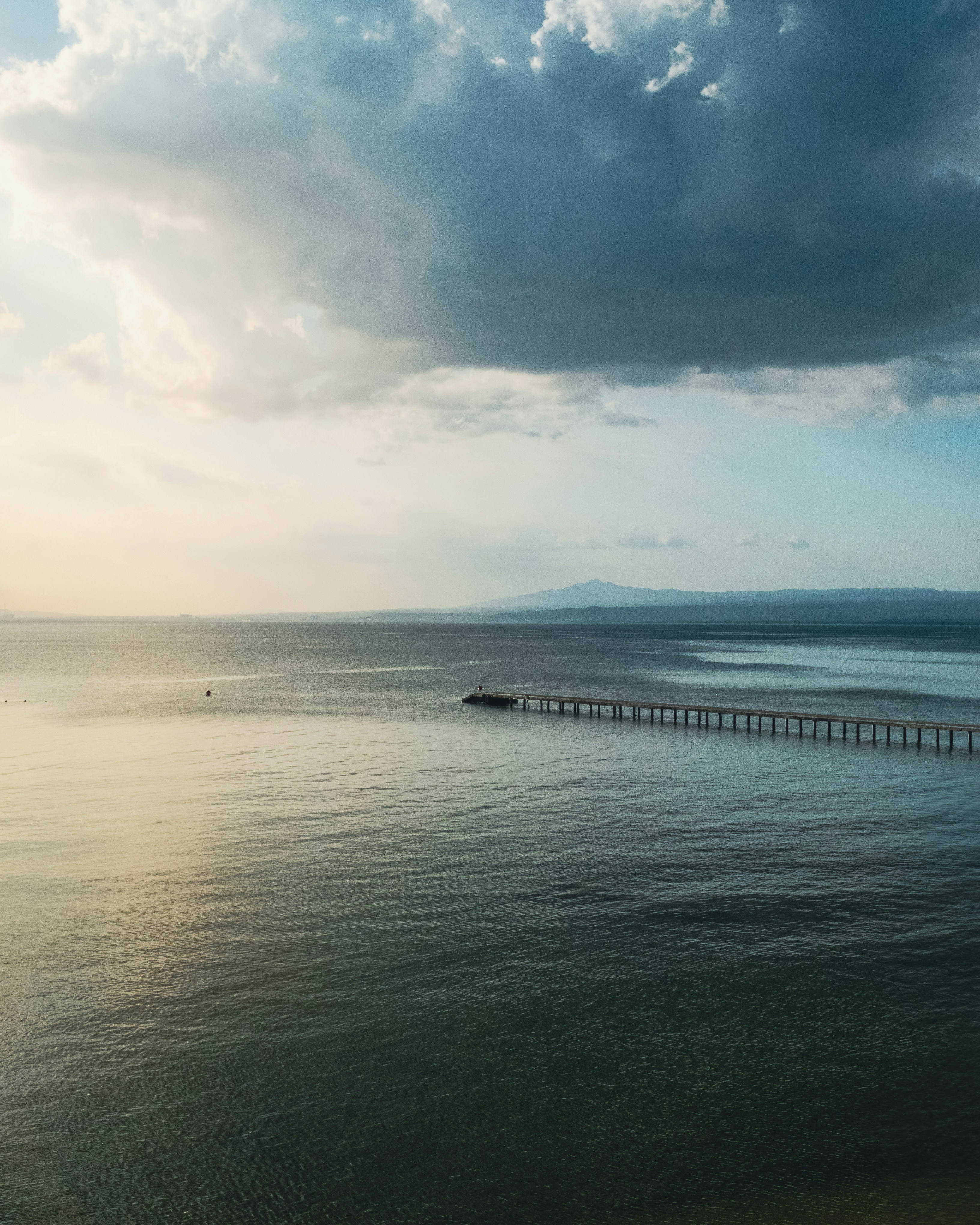 Dermaga panjang di atas air yang tenang dengan langit mendung.