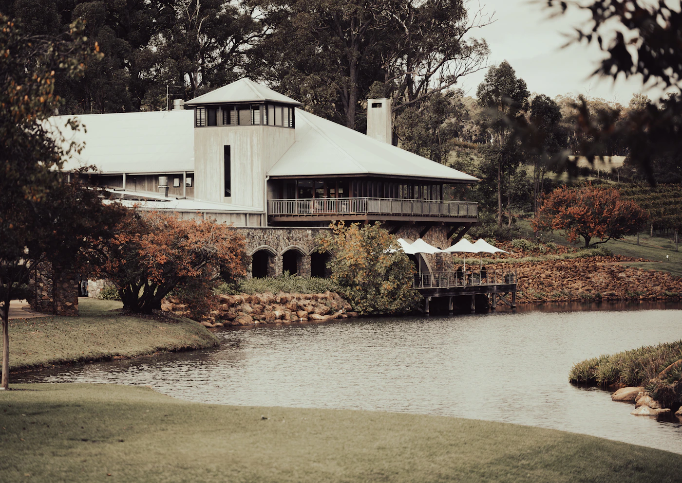 A resort and estate building set back from a calm lake or pond in autumn, the building reflected in still water with trees in fall colour surrounding the grounds